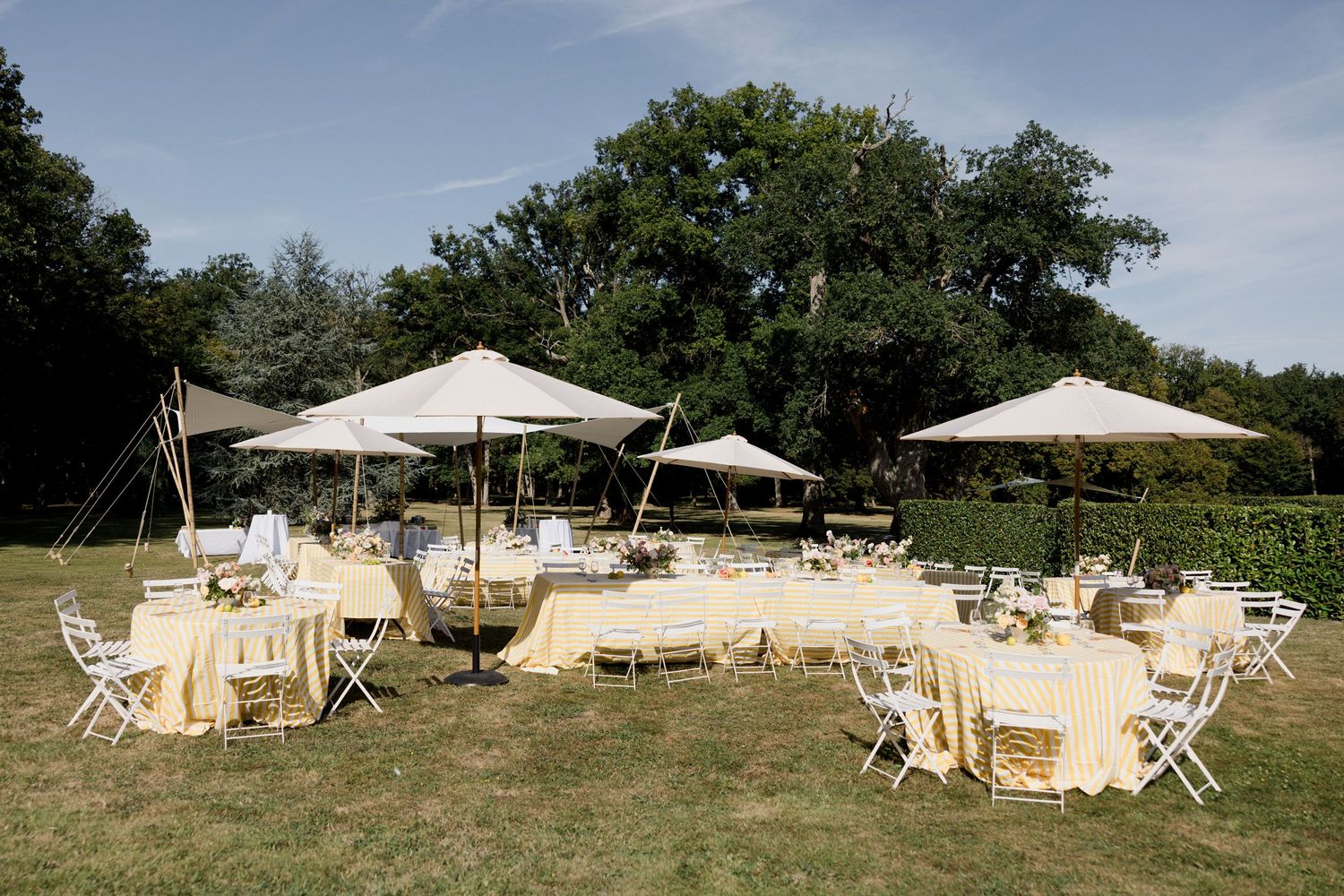 White outdoor lounge furniture and umbrellas arranged in a garden setting for an elegant event setup. Pool party loire valley