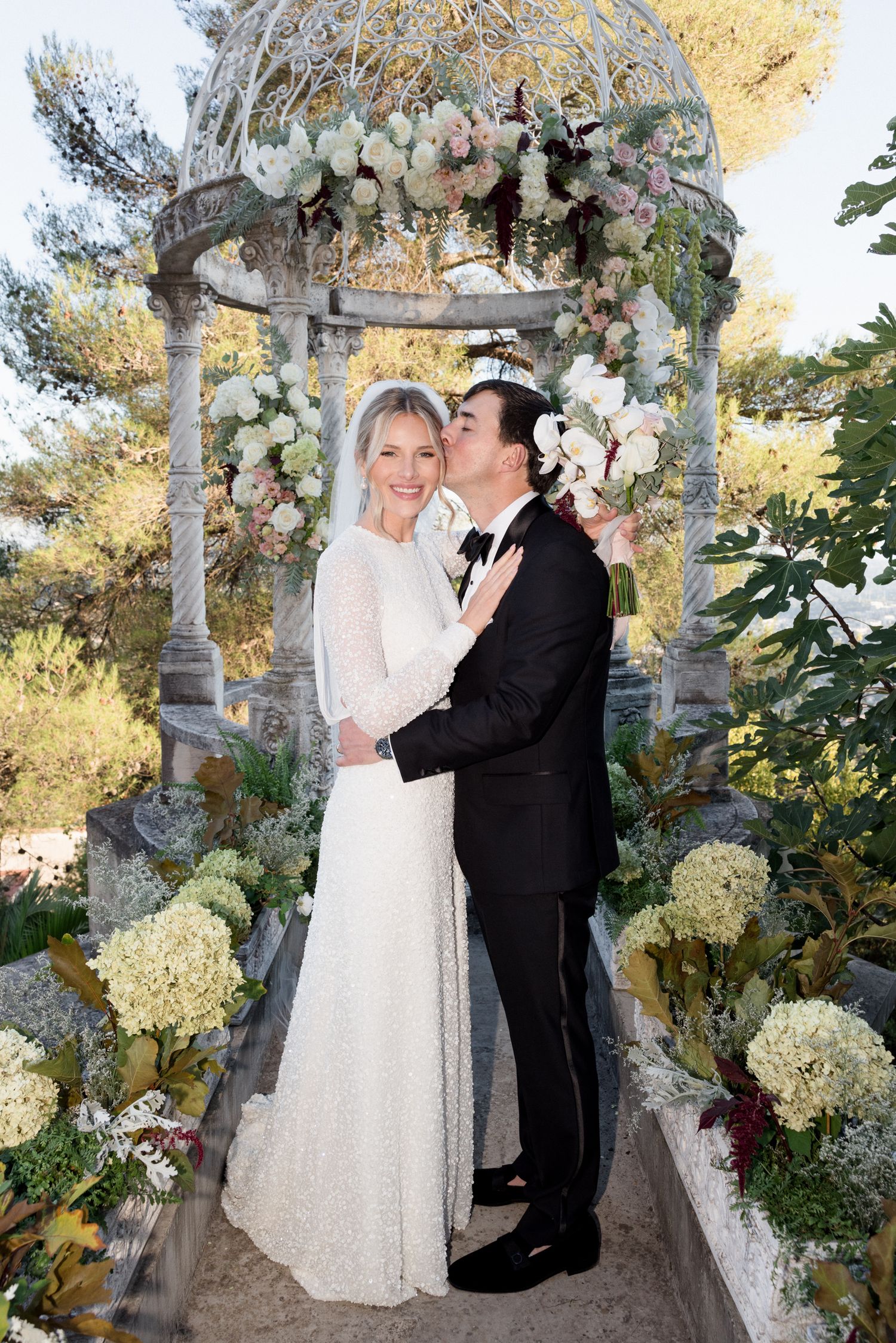 A romantic wedding moment captured under a floral-adorned gazebo with white hydrangeas and greenery. Intimate wedding french riviera