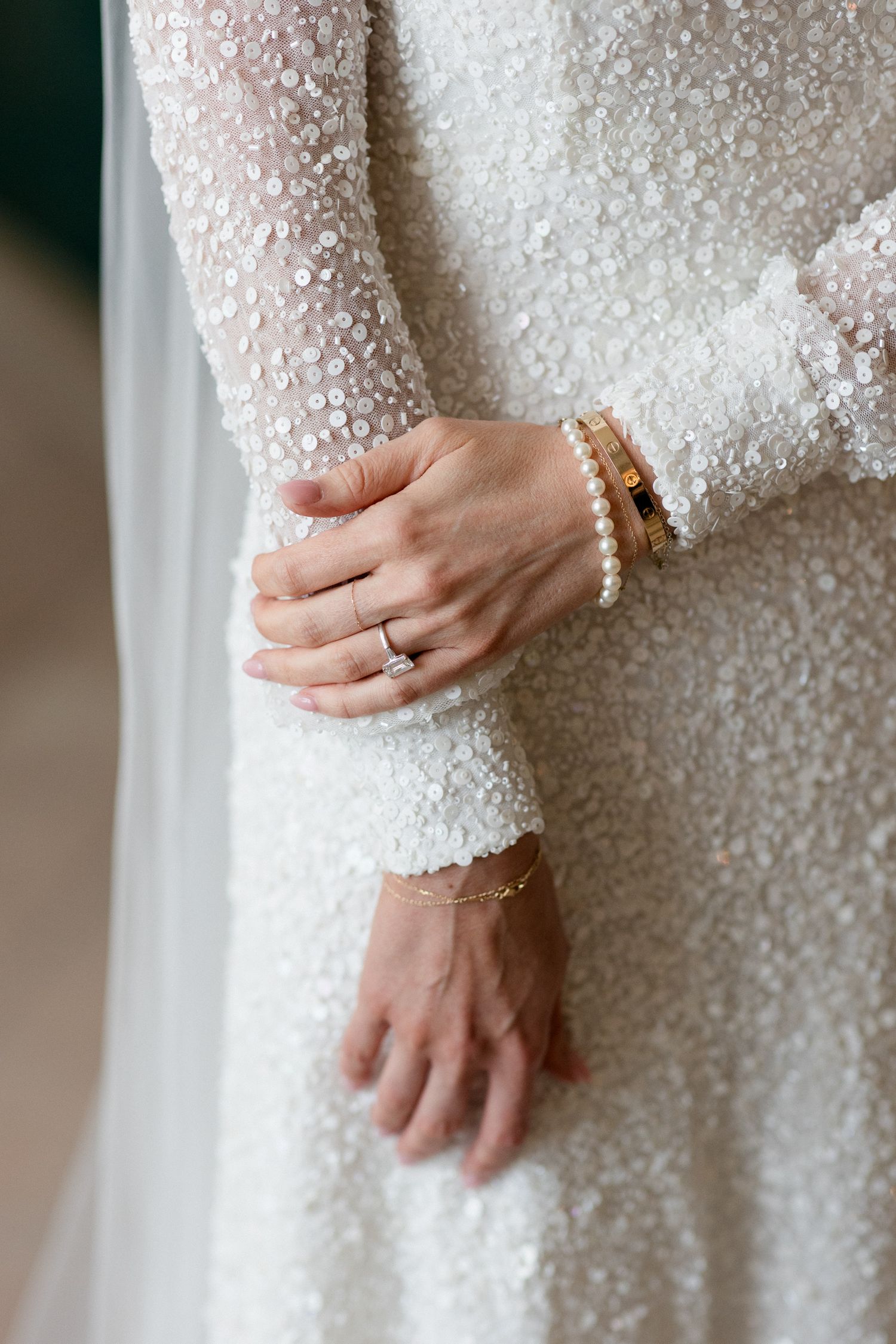 Close-up details of a sequined white wedding dress sleeve with delicate beading and a pearl bracelet.