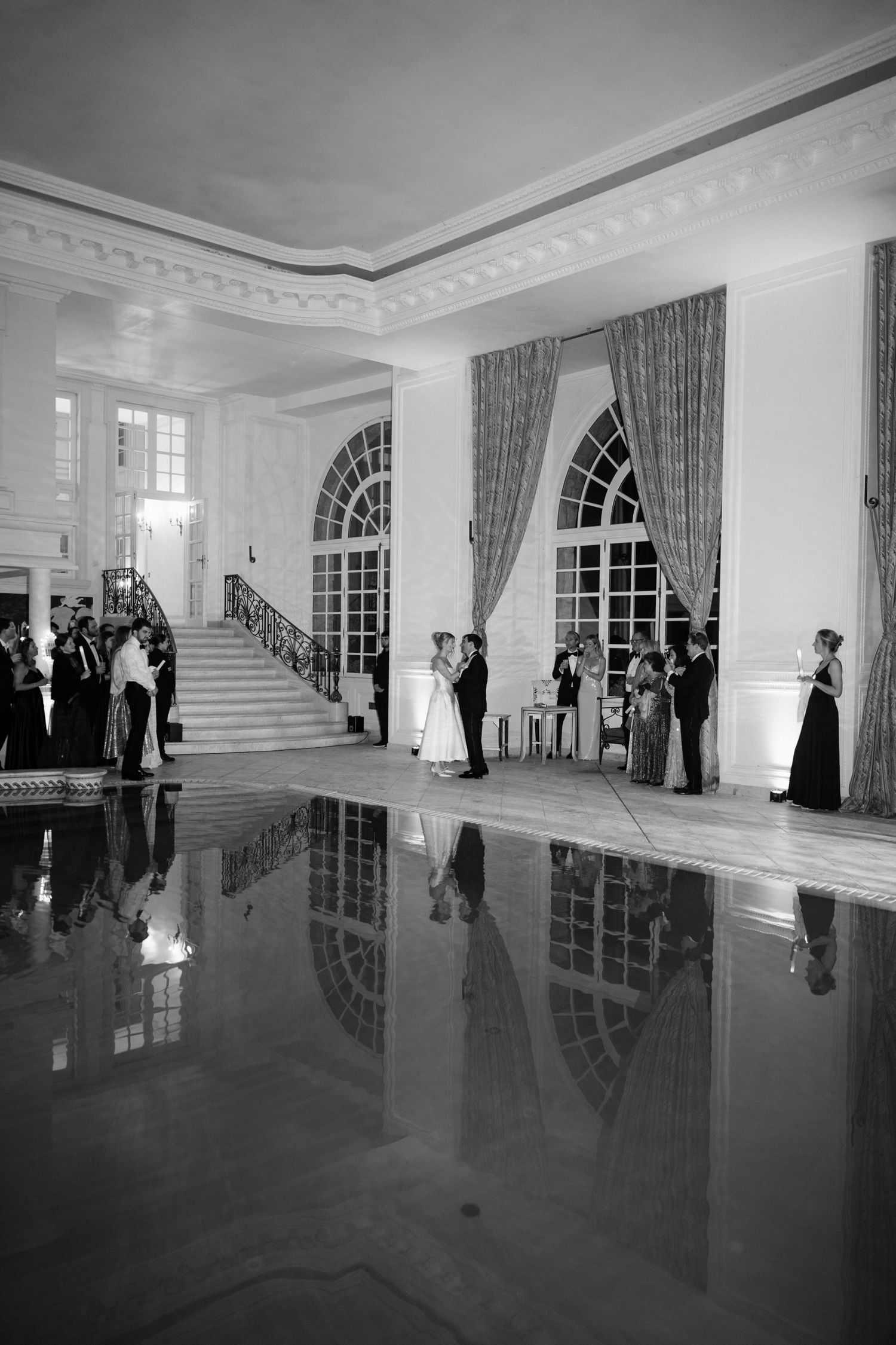 Black and white panoramic view of an elegant ballroom interior with reflective floors and French windows.