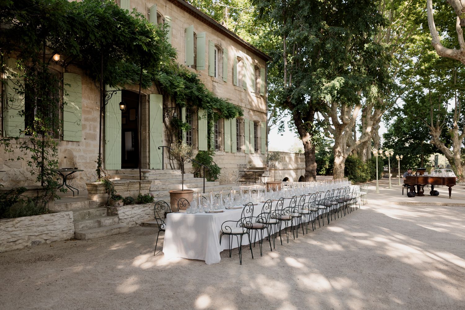 Long white table setup for outdoor wedding reception in front of a rustic Provencal stone house with climbing vines. Auberge de la treille