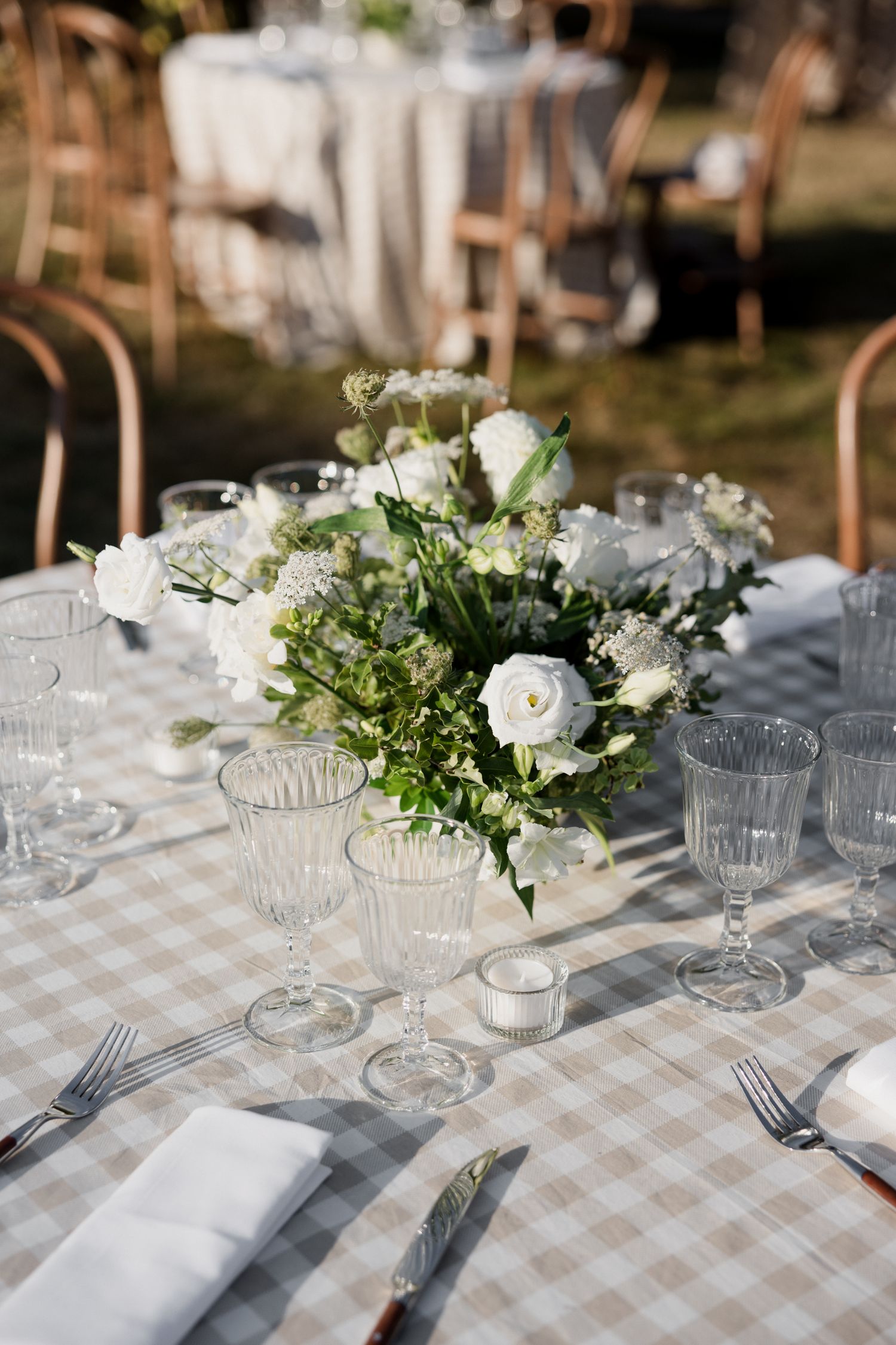 Elegant wedding table setting with white roses, gingham tablecloth, crystal glasses and greenery centerpieces.