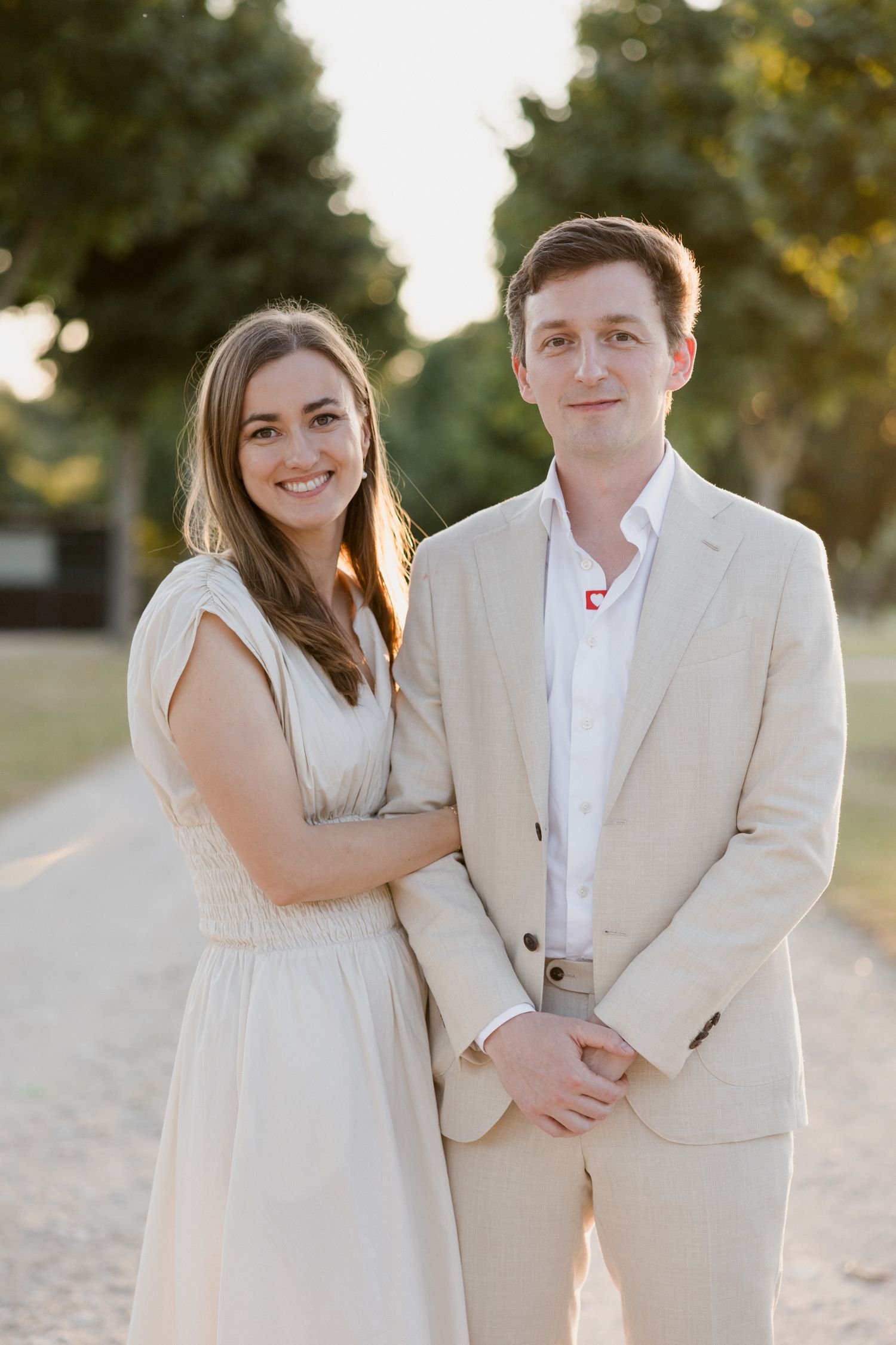 A couple in light beige and white outfits pose together for romantic sunset beach engagement photos. Photographe mariage Tours
