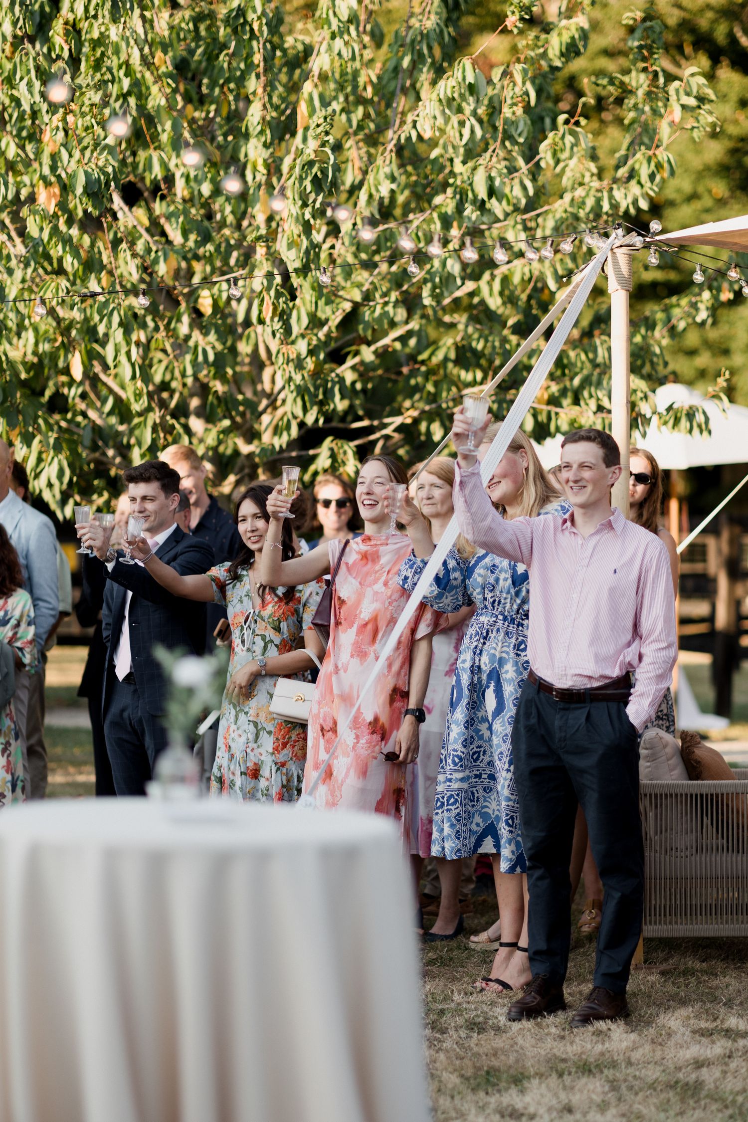 Wedding guests hold sparklers in a line outdoors during an evening celebration under trees.