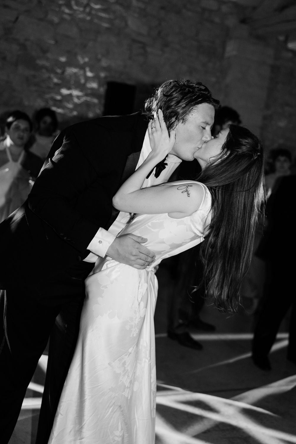 A couple dips and embraces while dancing at a wedding reception in a dimly lit venue.
