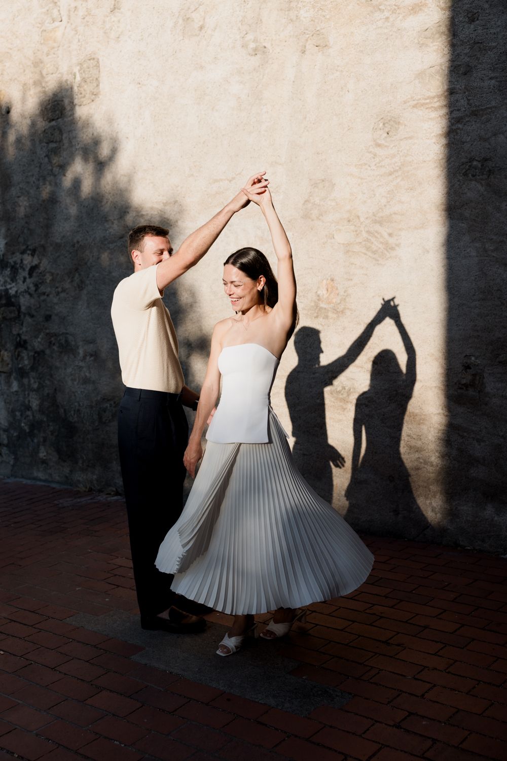 Couple dancing in sunlight casting dramatic shadows against a wall. Engagement session in Tours, Loire Valley