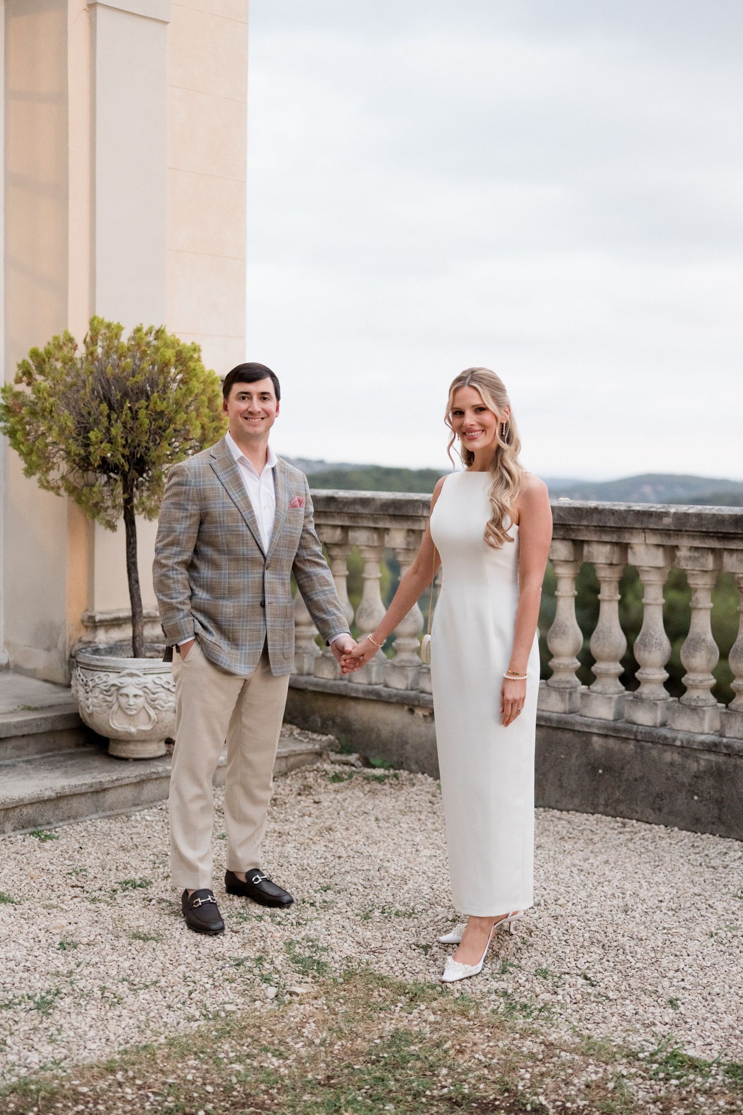 A romantic couple poses on a stone terrace with a scenic countryside backdrop during a wedding photo session.