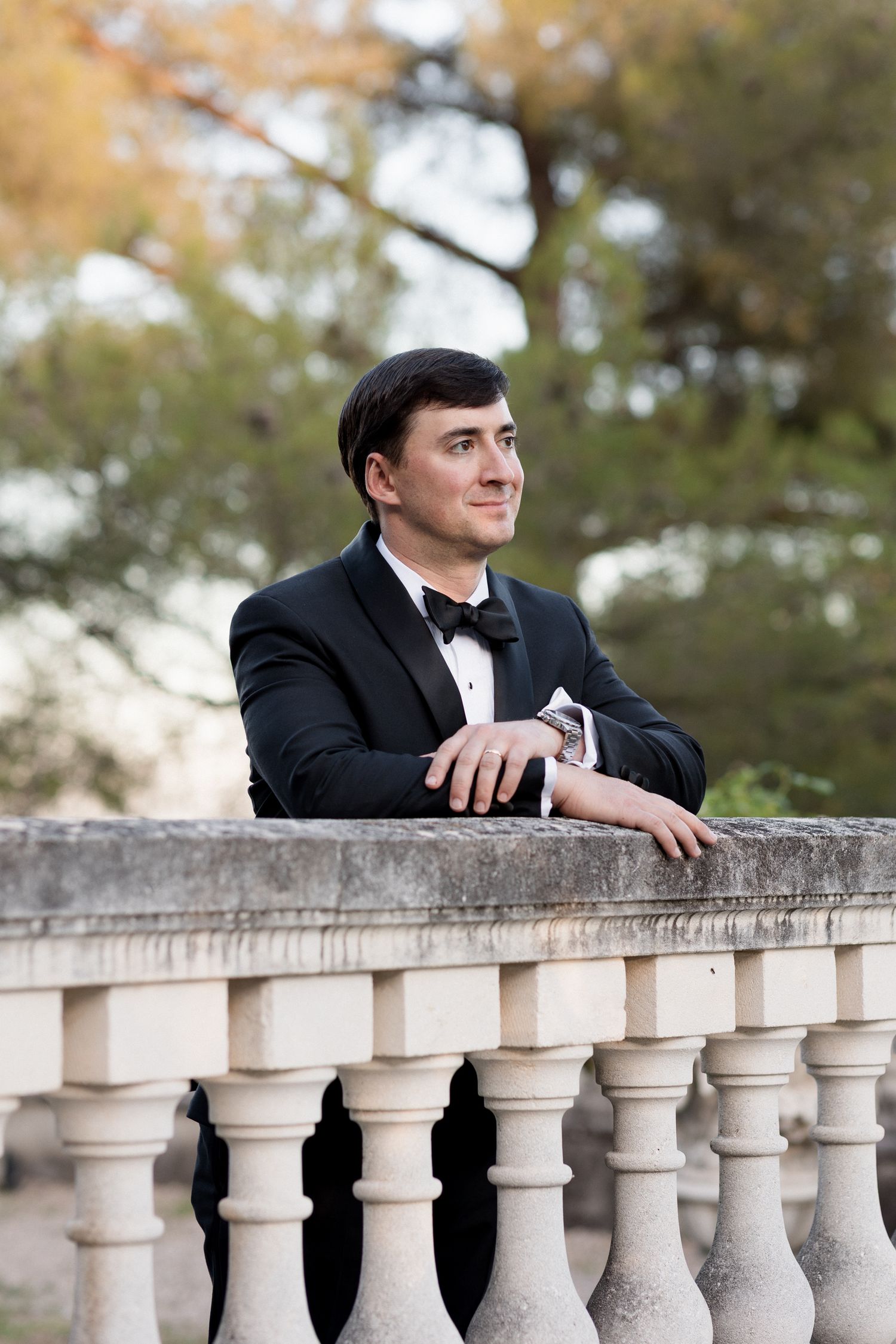 A person in formal attire leans on an ornate white stone balustrade in an outdoor setting. Photographe mariage provence