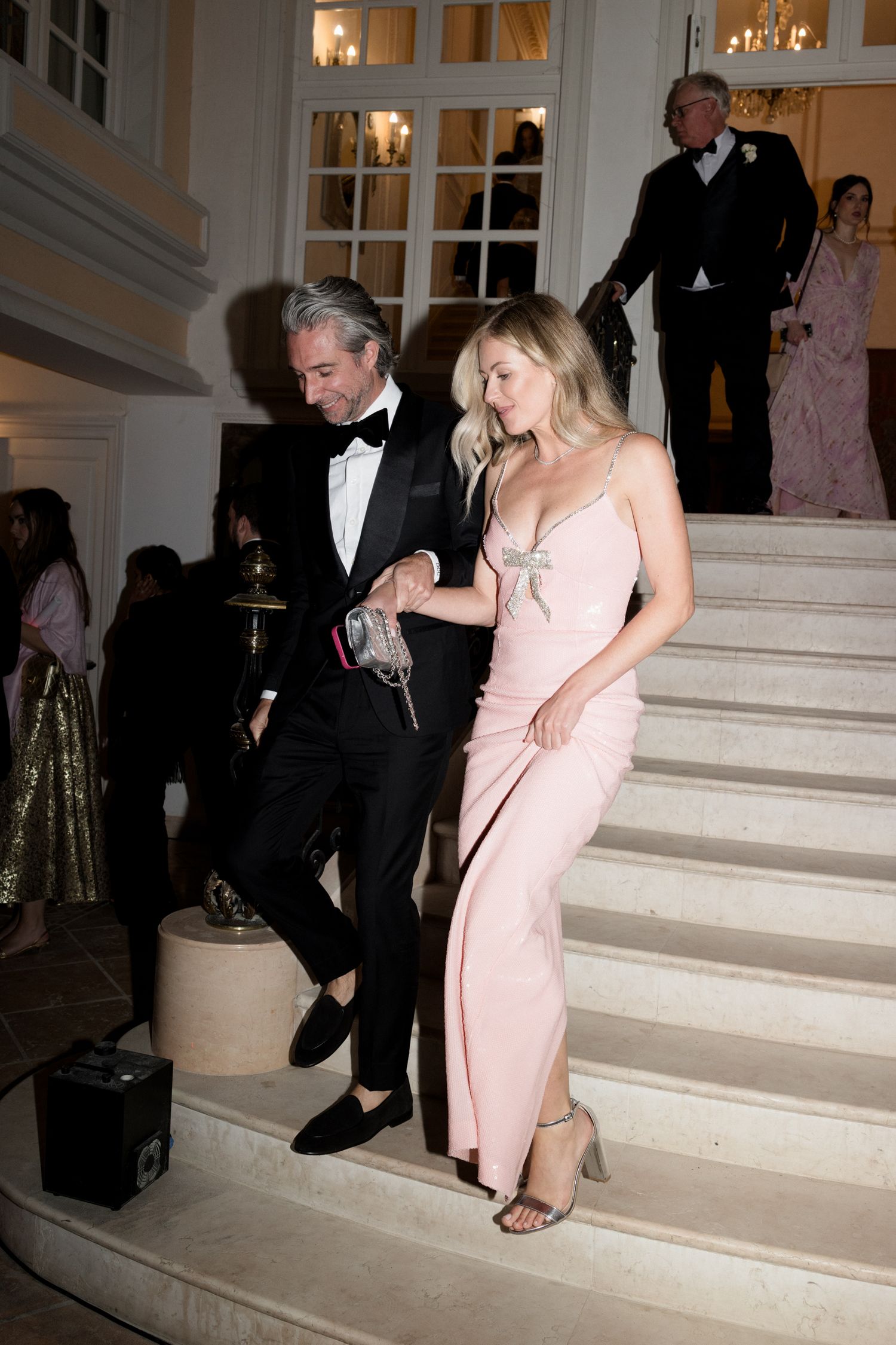 A sequence of photos showing a couple descending marble stairs at a formal event in black tie and pink dress attire.