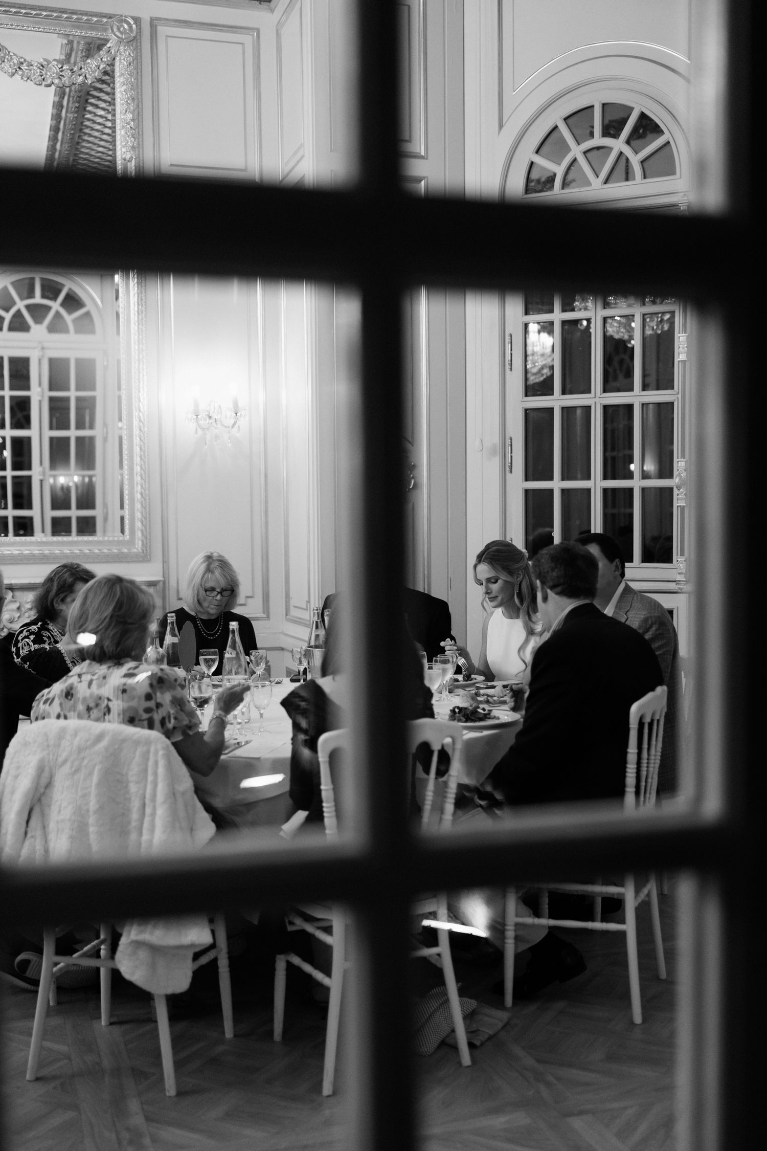 Black and white view through window bars of an elegant dining room with people seated at tables.