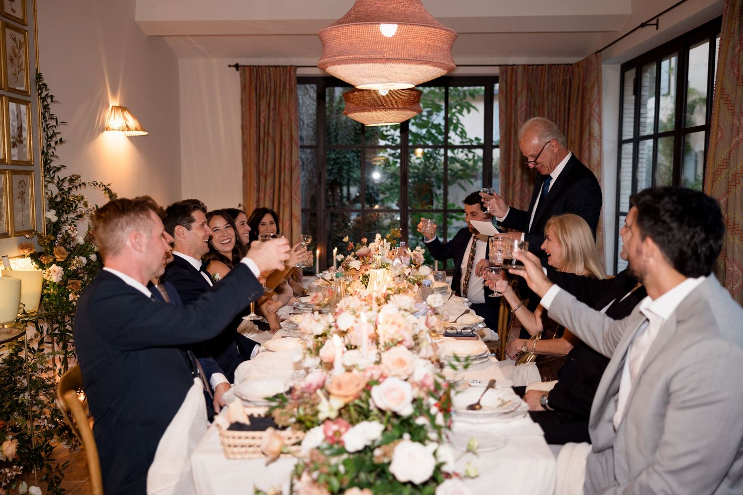 Wedding reception guests dine at elegant tables adorned with pink and white floral centerpieces and soft lighting.