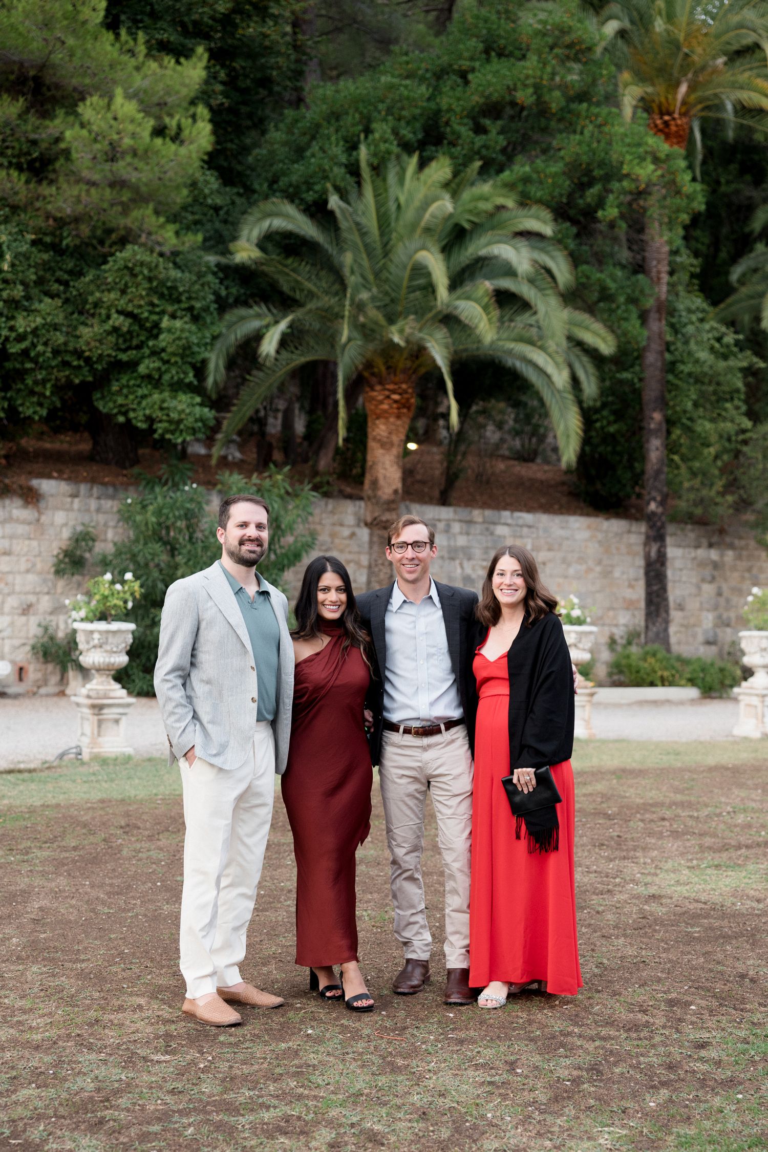 A group of people standing together outdoors in front of palm trees and a stone wall.
