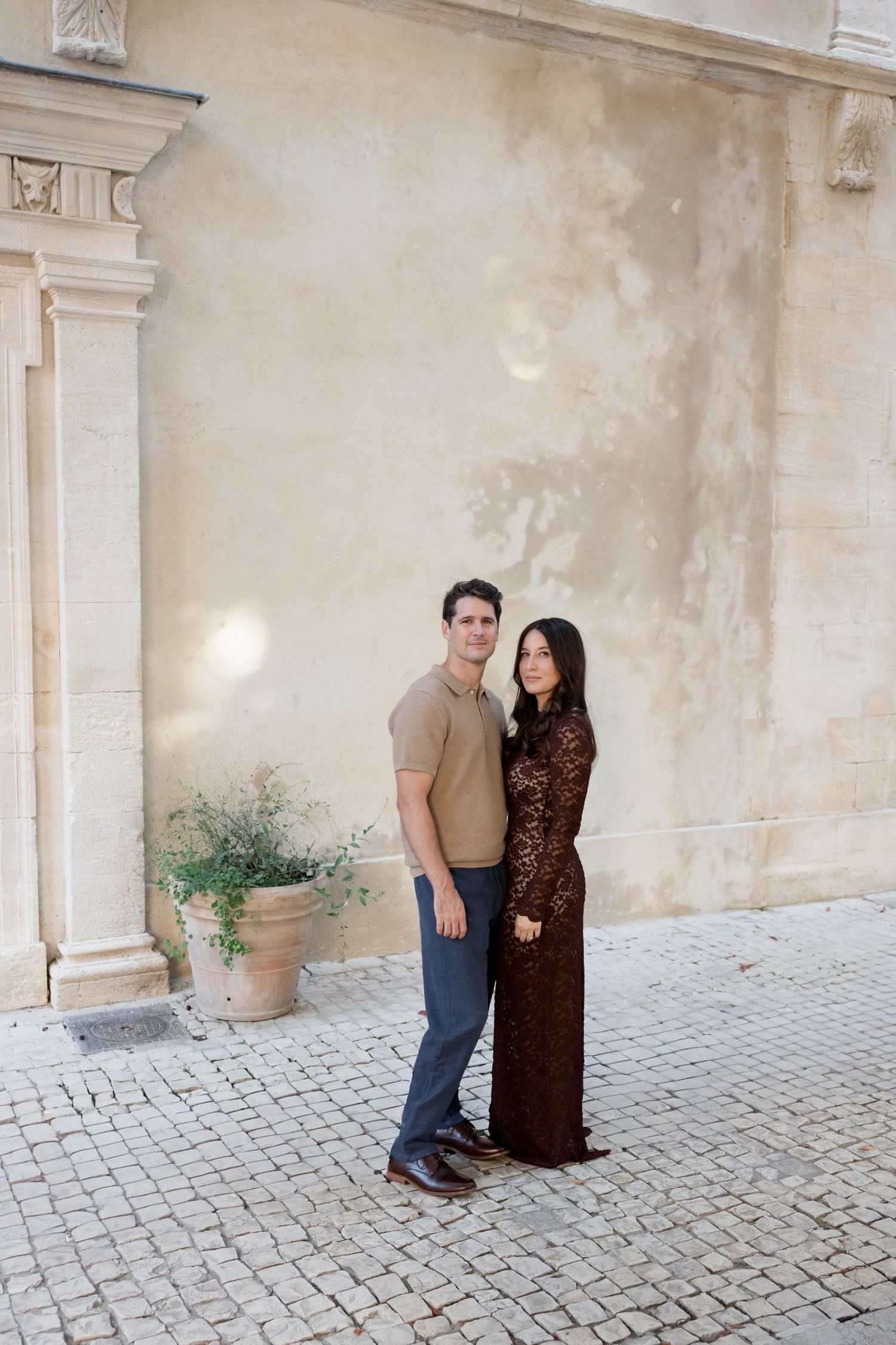 A couple poses together in a courtyard with stone walls and cobblestone pavement. Engagement session Paris