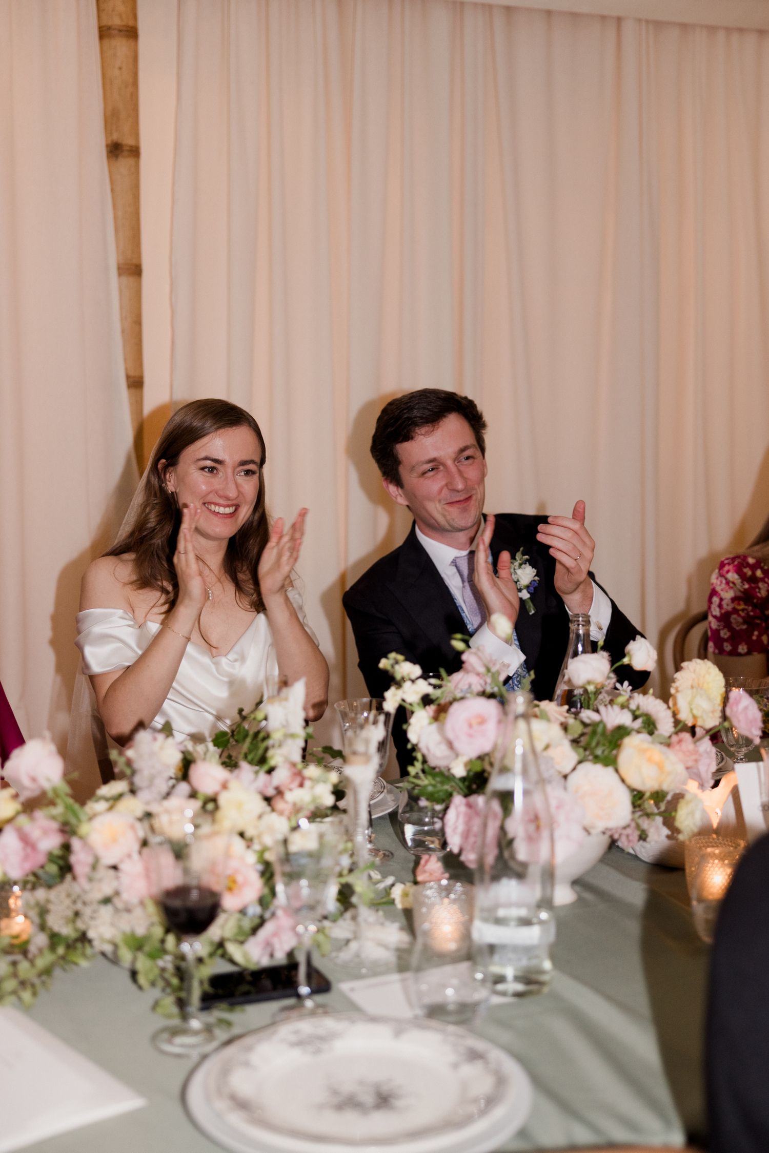 Wedding reception guests seated at a long table with elegant floral centerpieces and glowing candlelight.