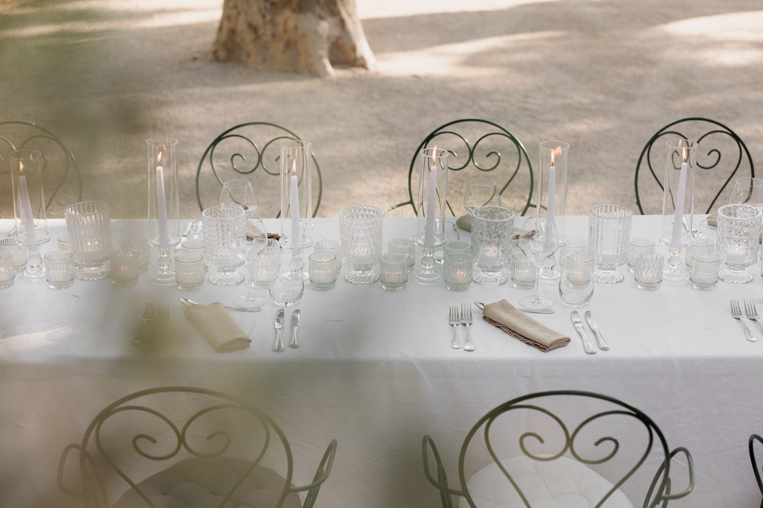 Clear glass tableware and white wrought iron chairs set up for an elegant outdoor dining arrangement.