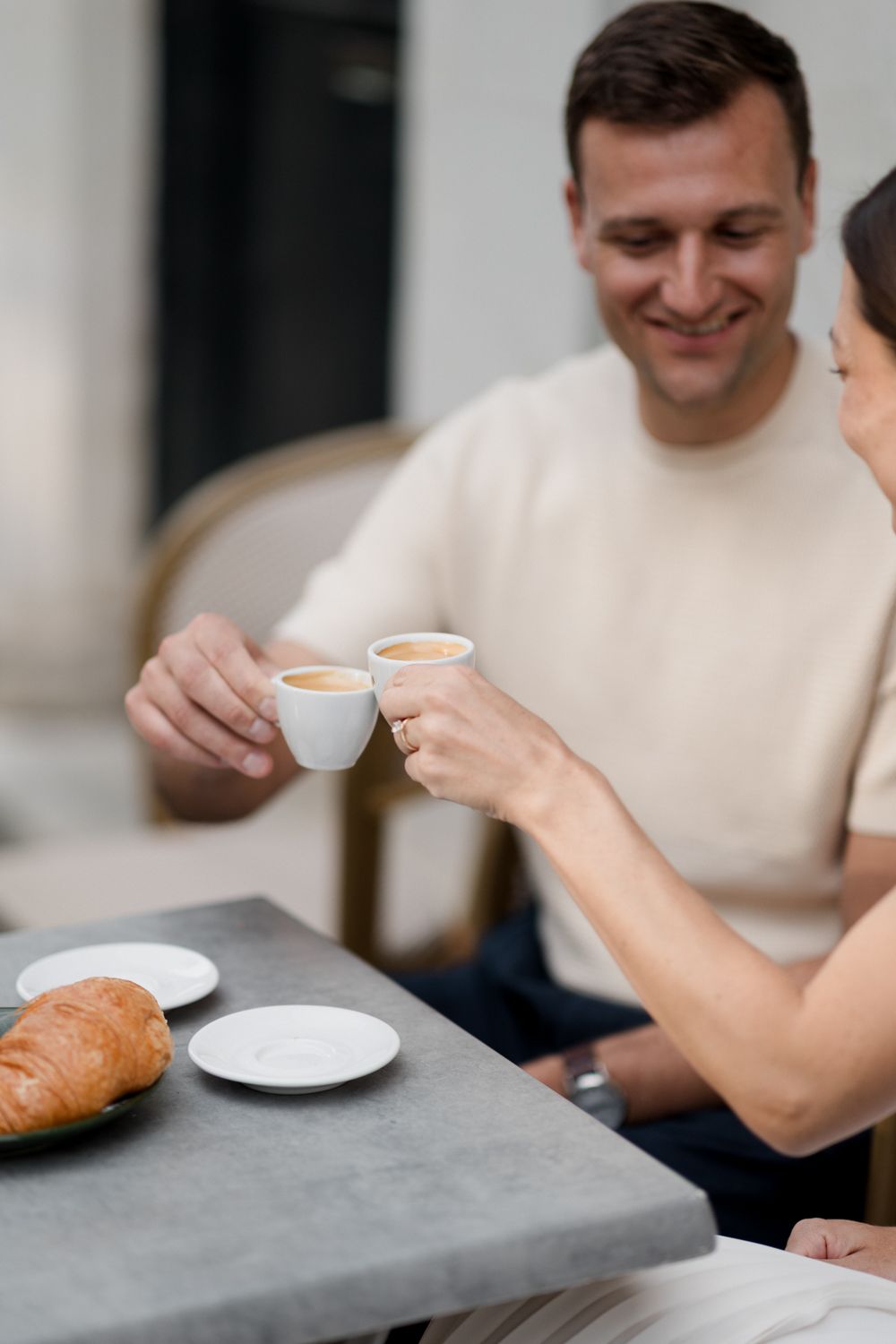Person in white top enjoying coffee at a gray table with a croissant in a modern setting.