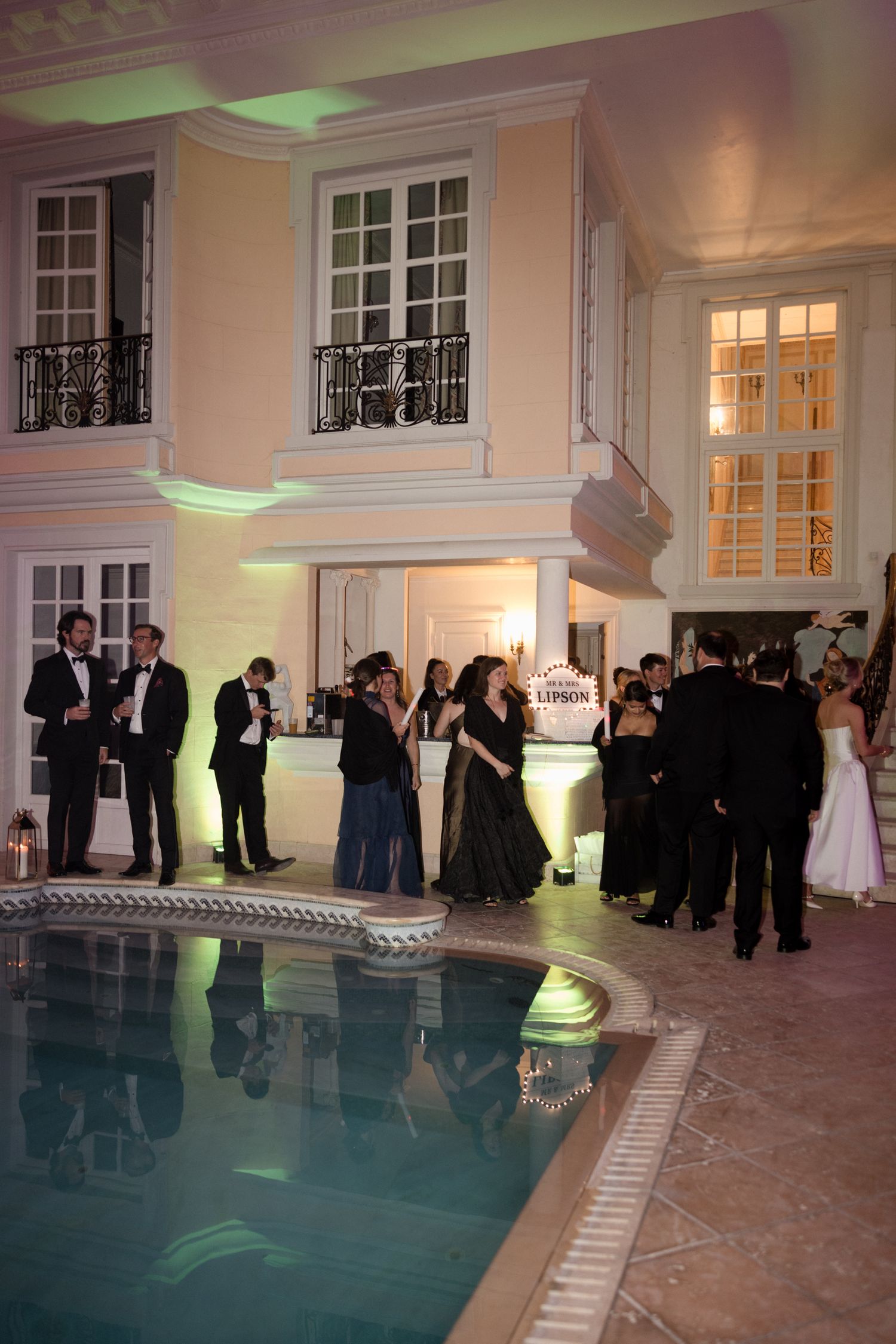 Elegant indoor pool area at a formal event with guests in black tie attire mingling around the illuminated water.