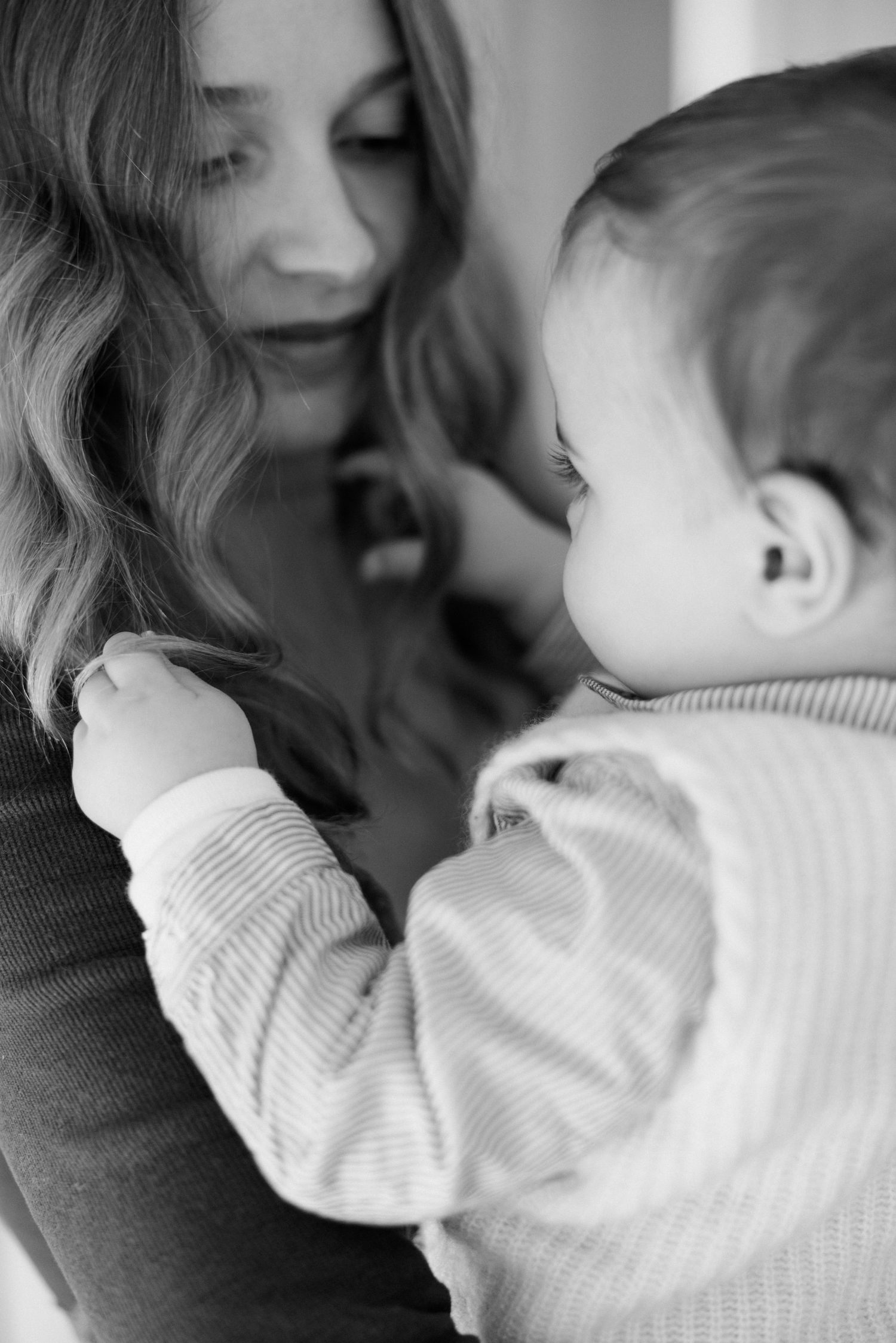 Black and white photo of a young mother lovingly gazing at her baby in a striped outfit.