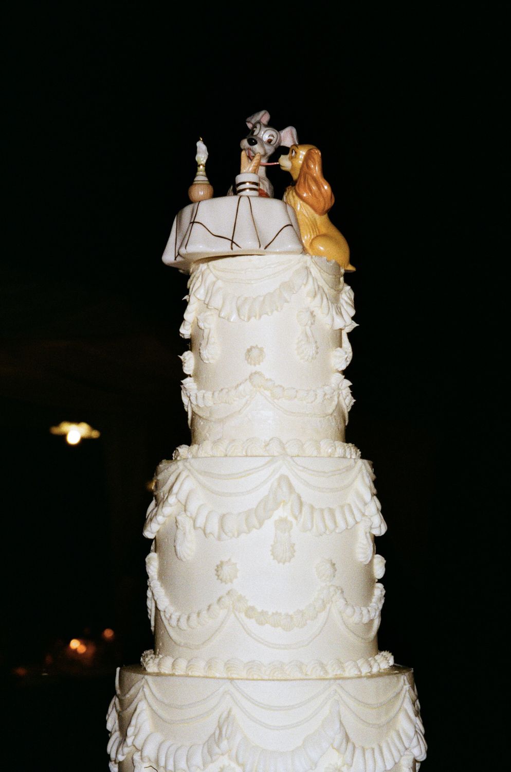 An elegant multi-tiered white wedding cake with intricate piped details and bride and groom topper displayed at a reception.