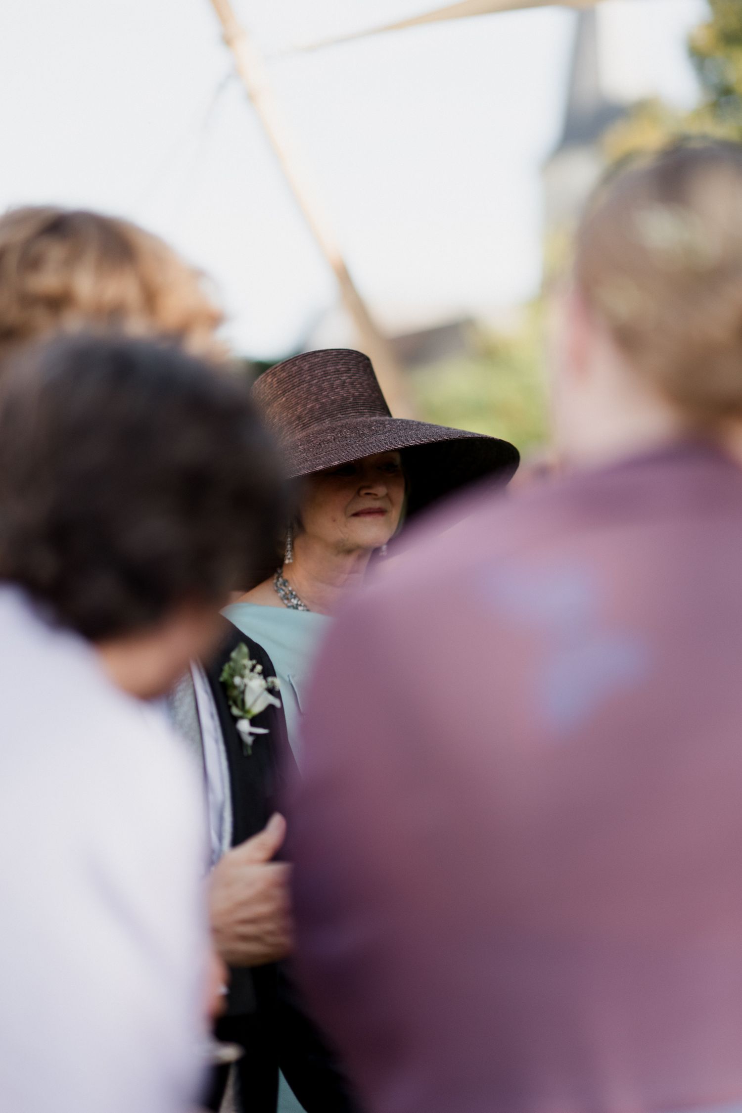 A person wearing a brown hat stands among a blurred crowd at an outdoor gathering.