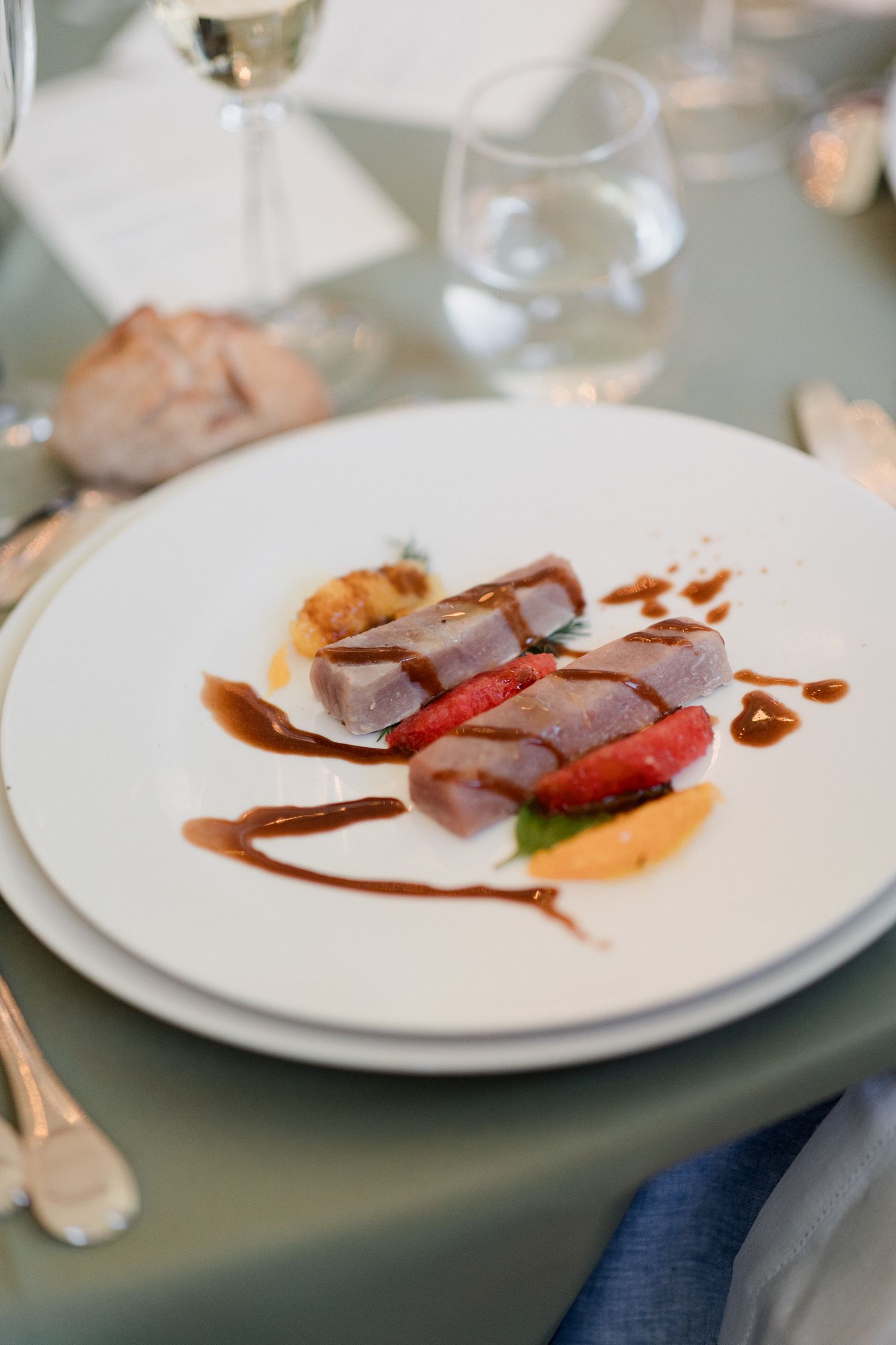 Elegant plated dish featuring sliced meat with strawberries and a rich brown sauce drizzle on white china.