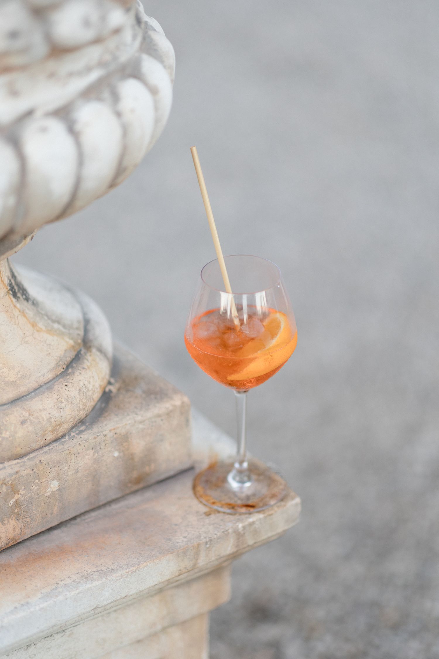 An orange cocktail in a stemmed wine glass sits on a stone ledge with a wooden straw. Photographe mariage provence