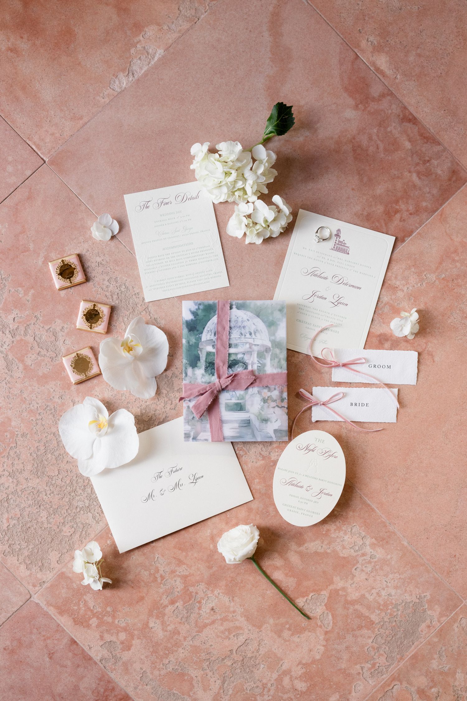 Elegant wedding stationery and invitations laid out on pink marble with delicate white flowers and vintage photographs. destination wedding
