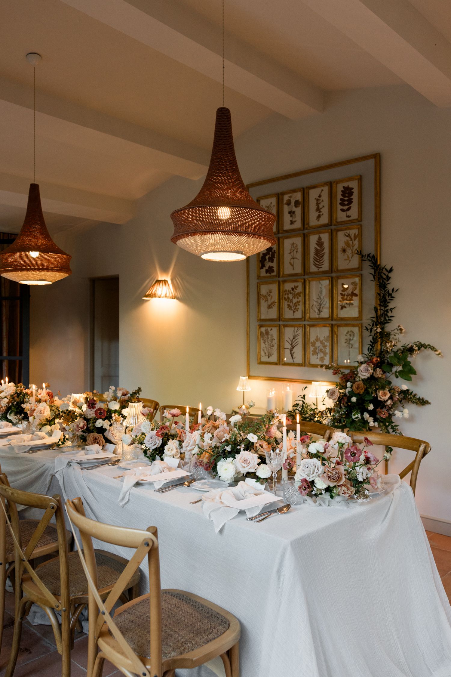 Elegant wedding reception table with rustic pendant lights and floral centerpieces under framed botanical prints.