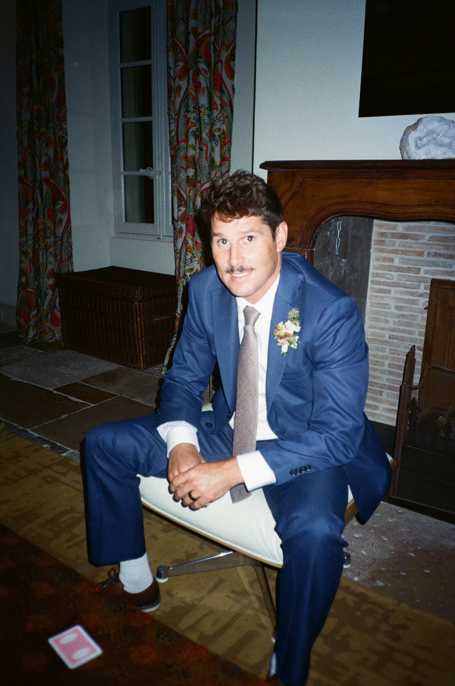 A person in a navy blue suit sits thoughtfully in a dimly lit room.