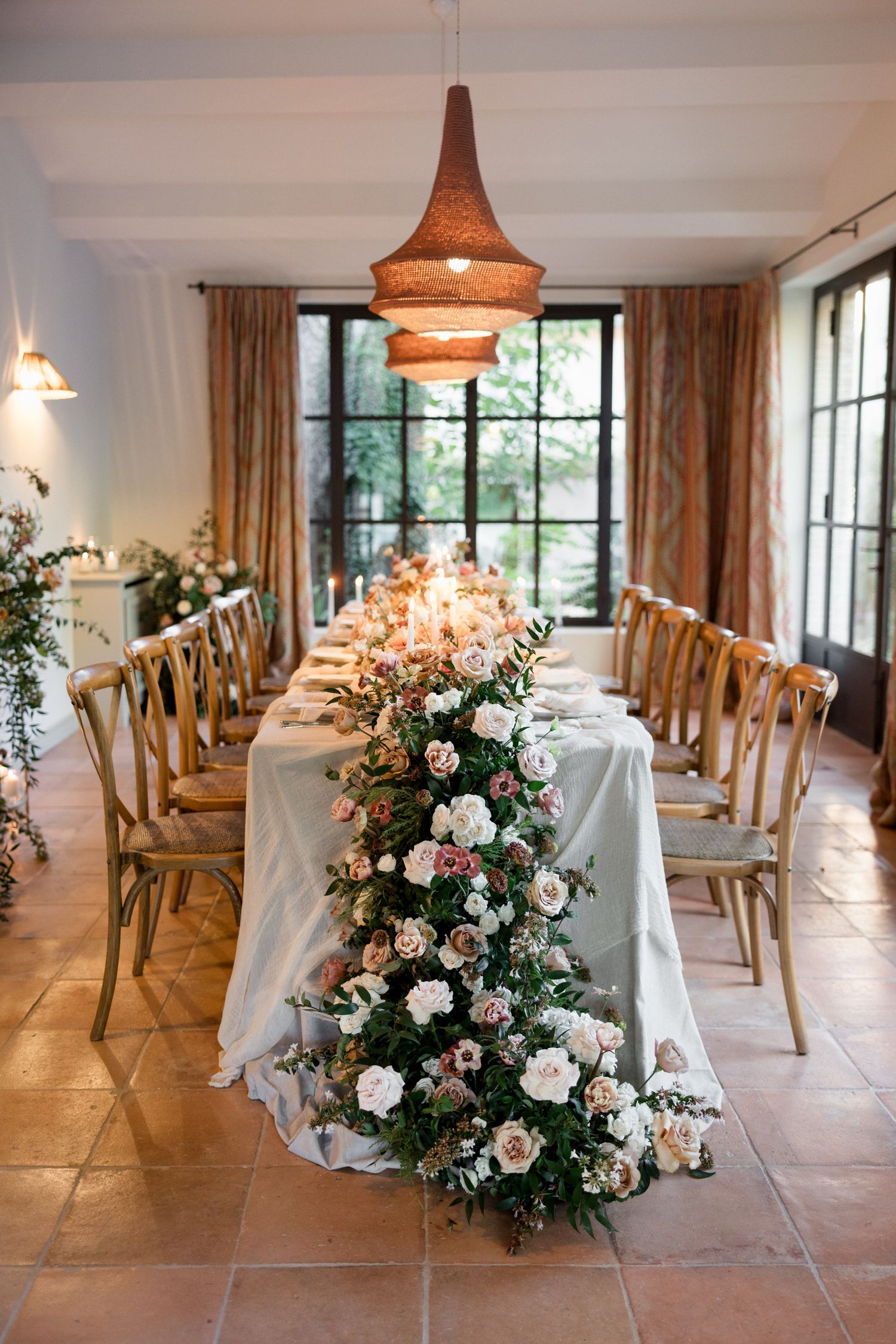 Elegant wedding reception venue with rustic wooden chairs, terracotta floors, and romantic floral centerpieces.