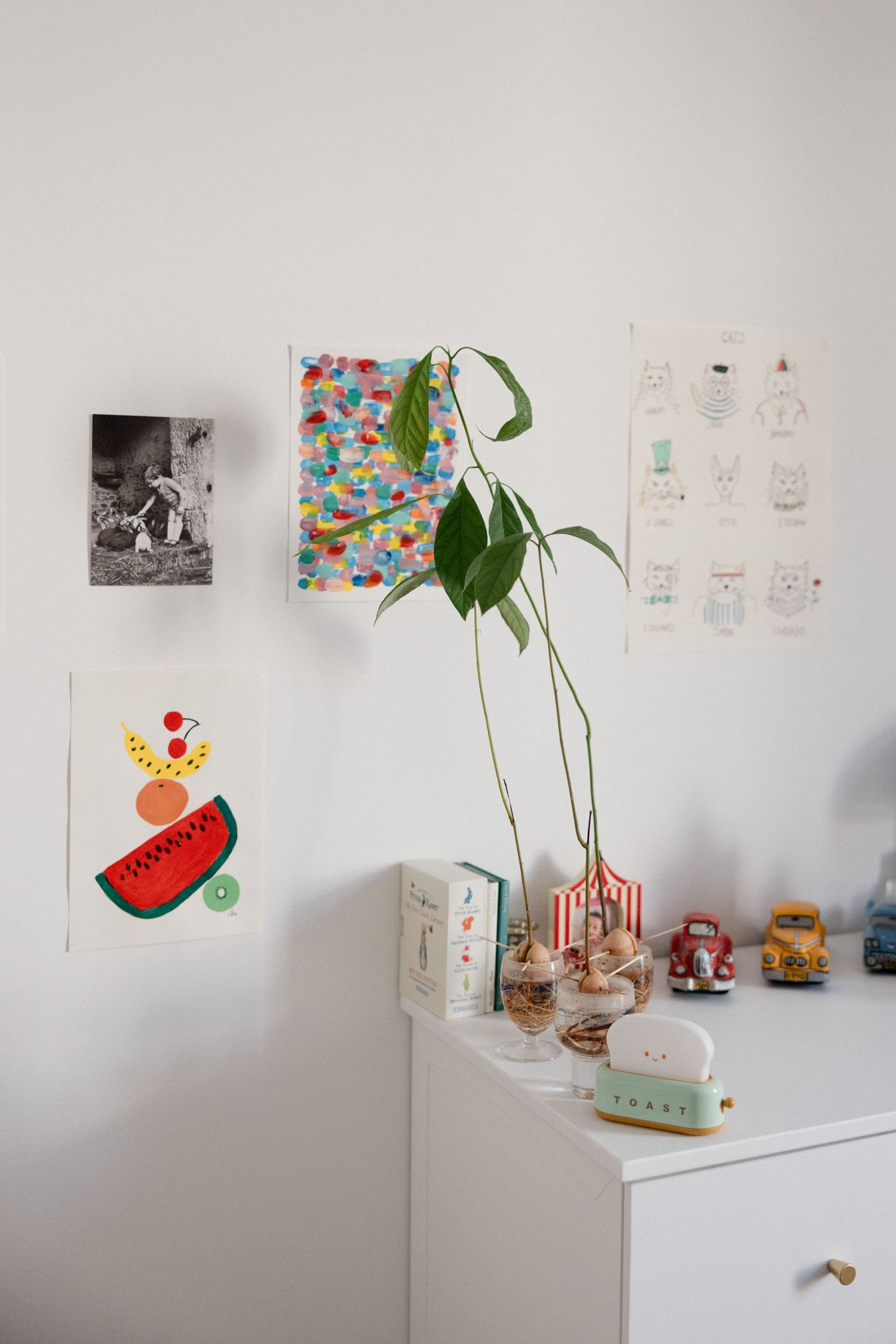 White dresser with plant, toys, and colorful art prints on wall in a bright, cheerful children's room.