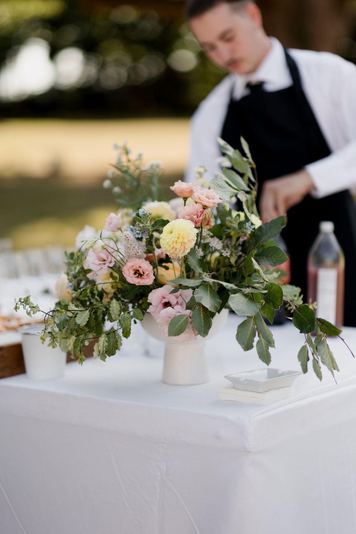Small floral centerpieces with pink and cream blooms and eucalyptus arranged in white vases on a white tablecloth. Paris wedding photographe