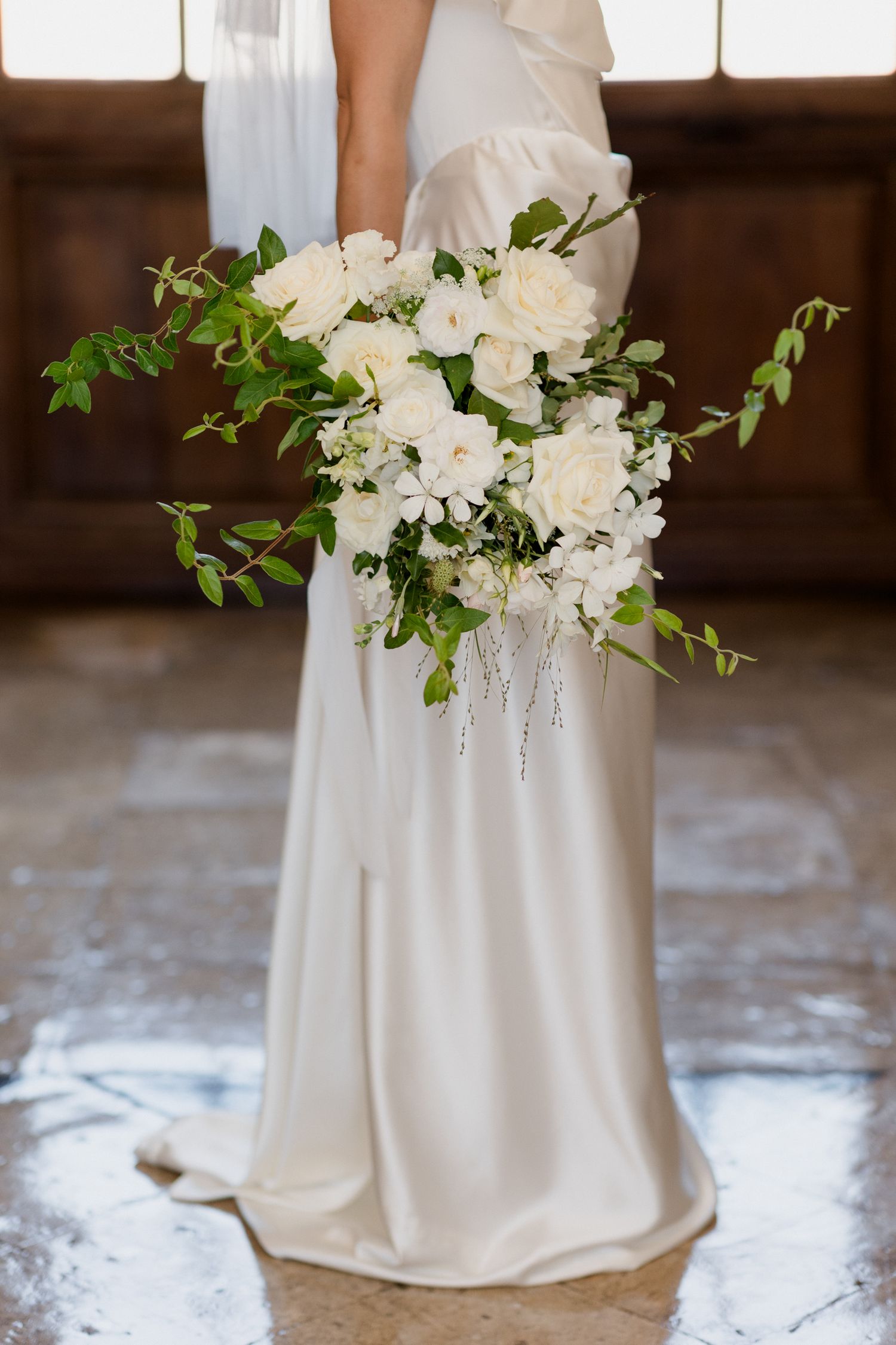Elegant white wedding dress with flowing fabric and delicate floral bouquet arrangement against rustic wooden backdrop.