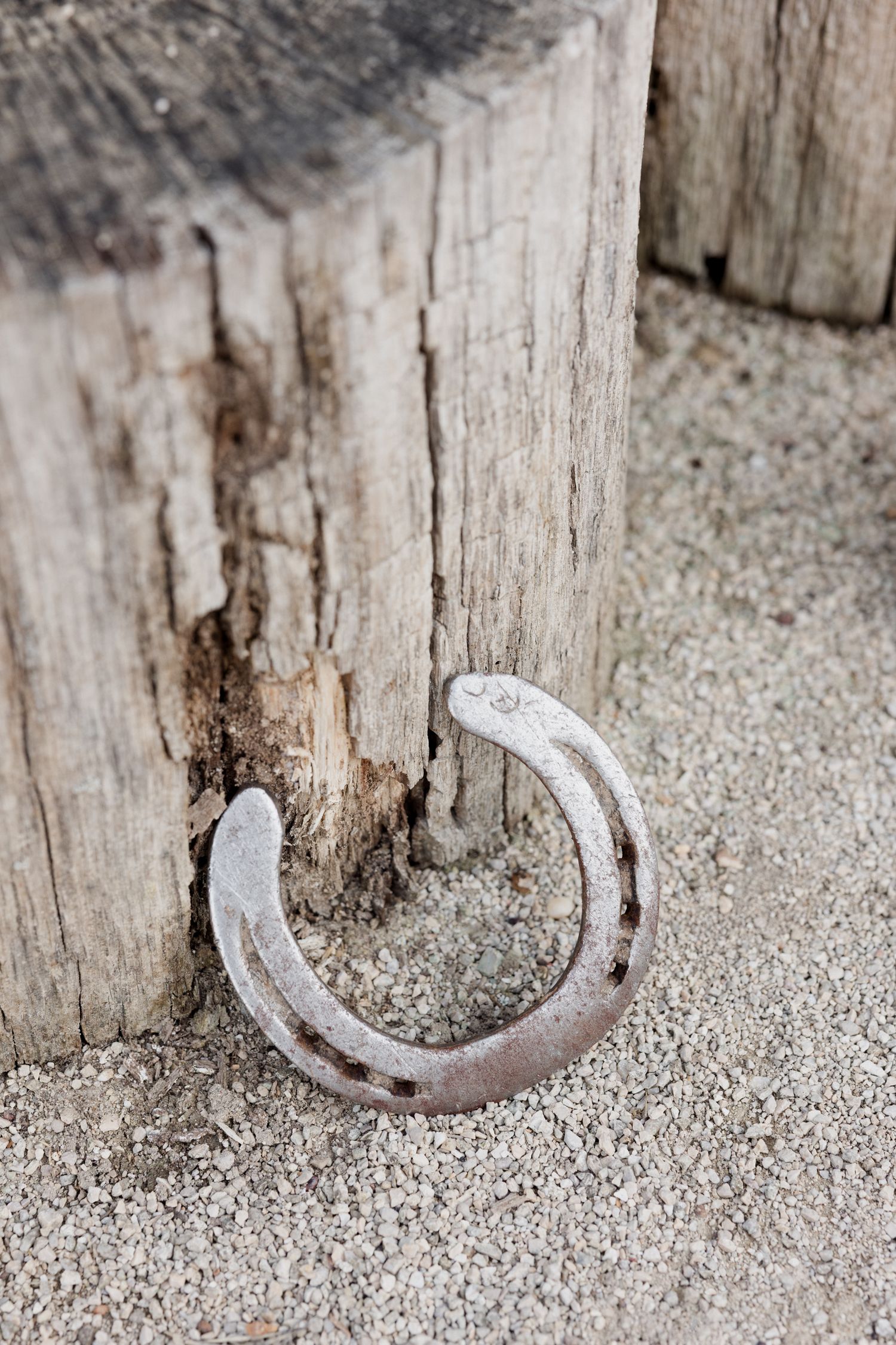 A rustic old horseshoe leans against a weathered wooden post on sandy ground in a close-up shot.