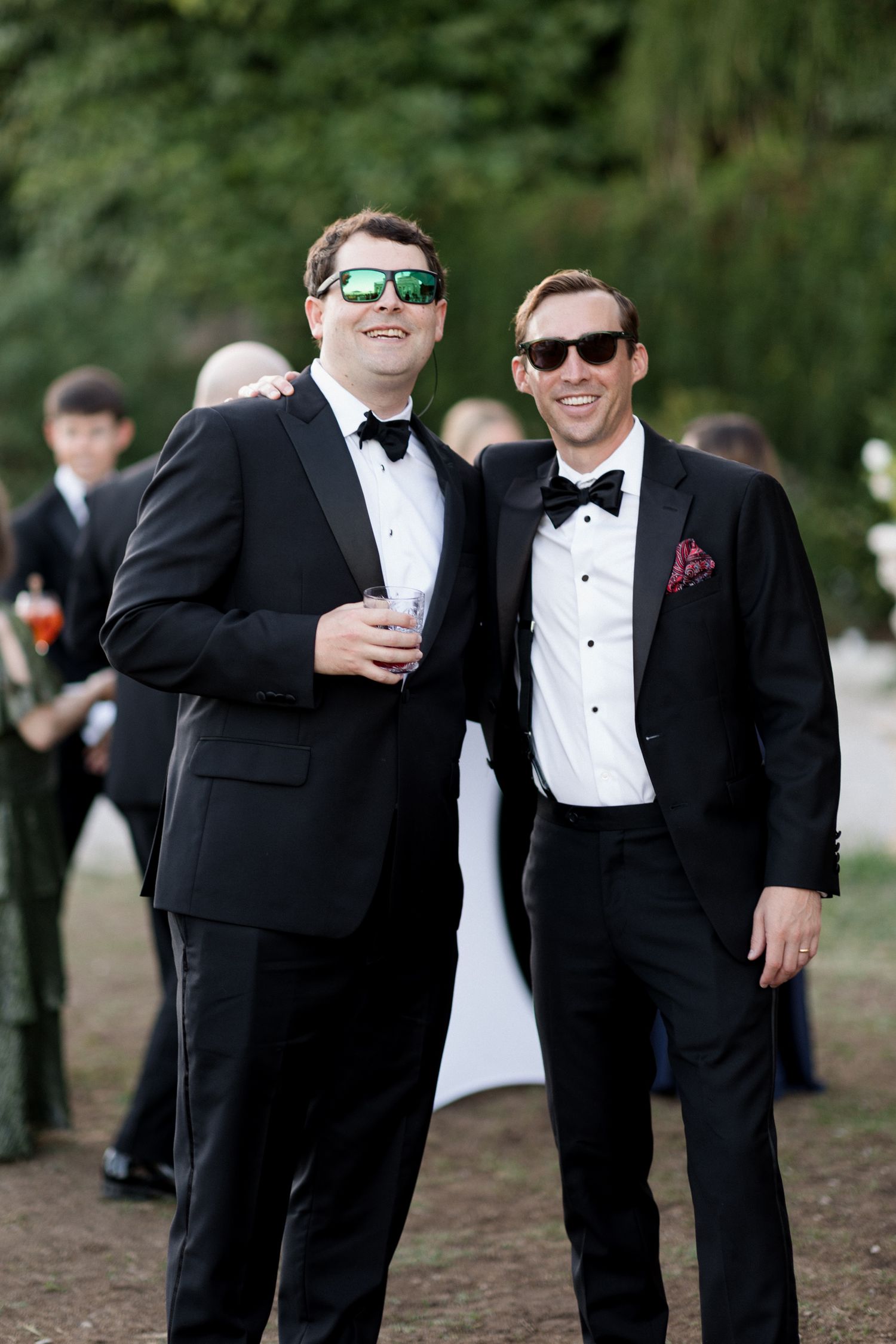 Groomsmen in black tuxedos and sunglasses pose together outdoors in a candid wedding photo series. Photographe mariage provence