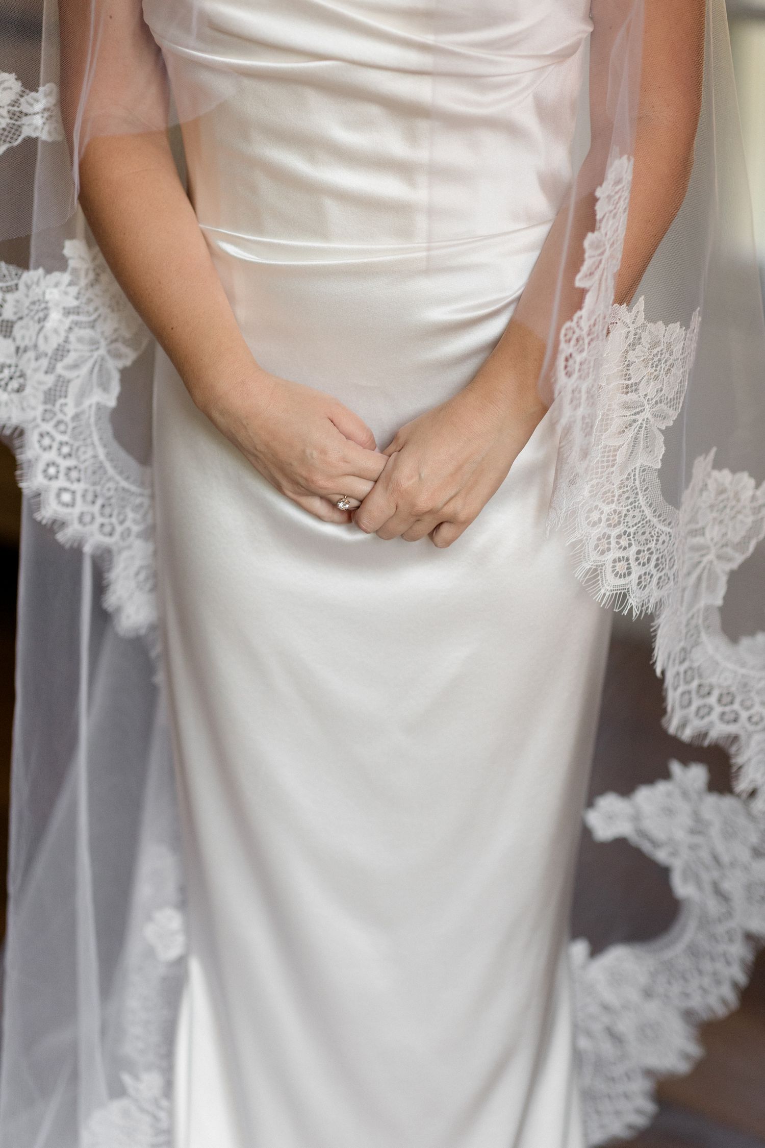 Close-up detail of a white satin wedding dress with delicate lace trim and gathered fabric at the waist. Editorial wedding photographer