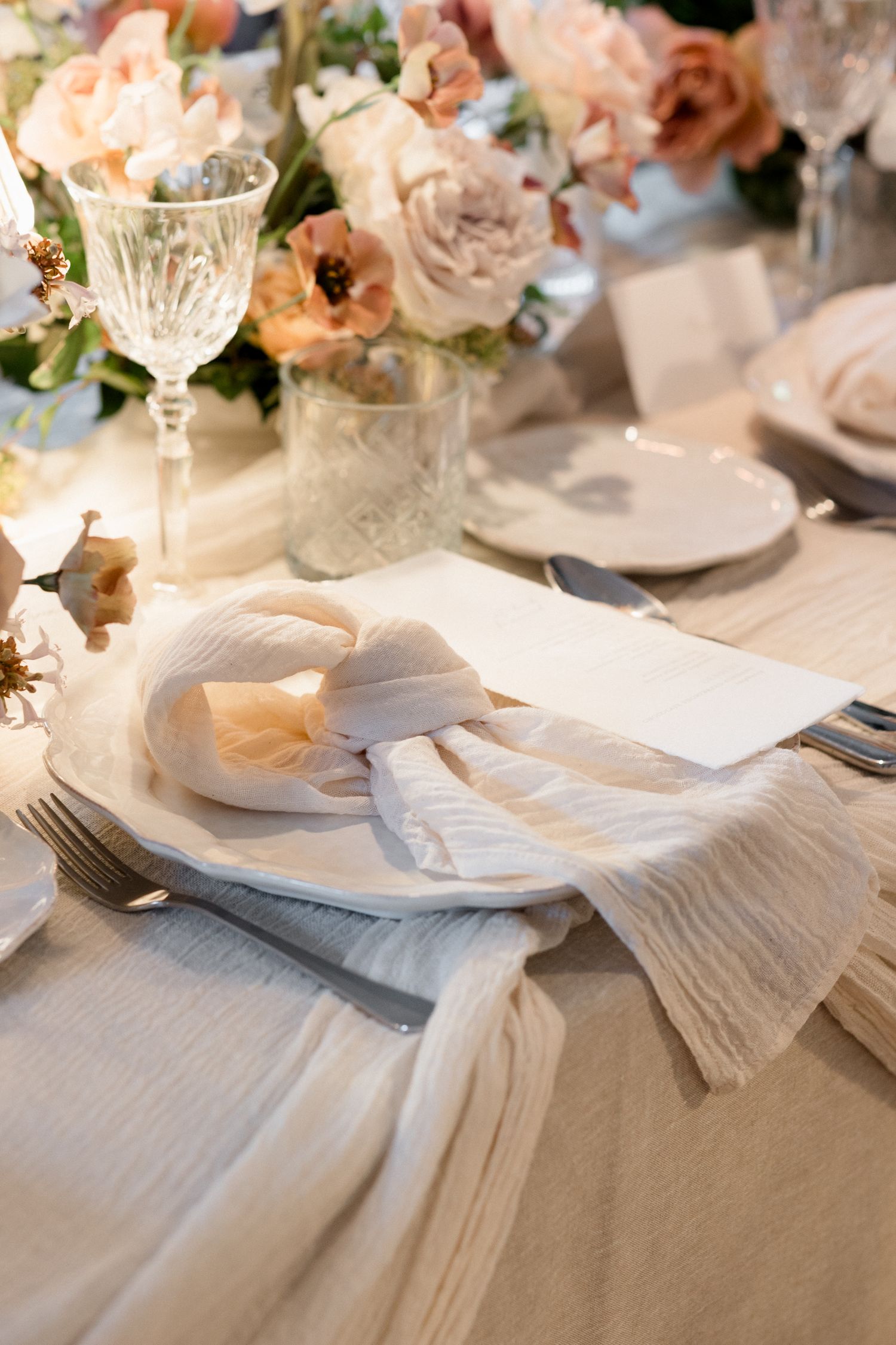 Elegant wedding table settings with white napkins, crystal glasses and soft pink floral arrangements create a romantic atmosphere.