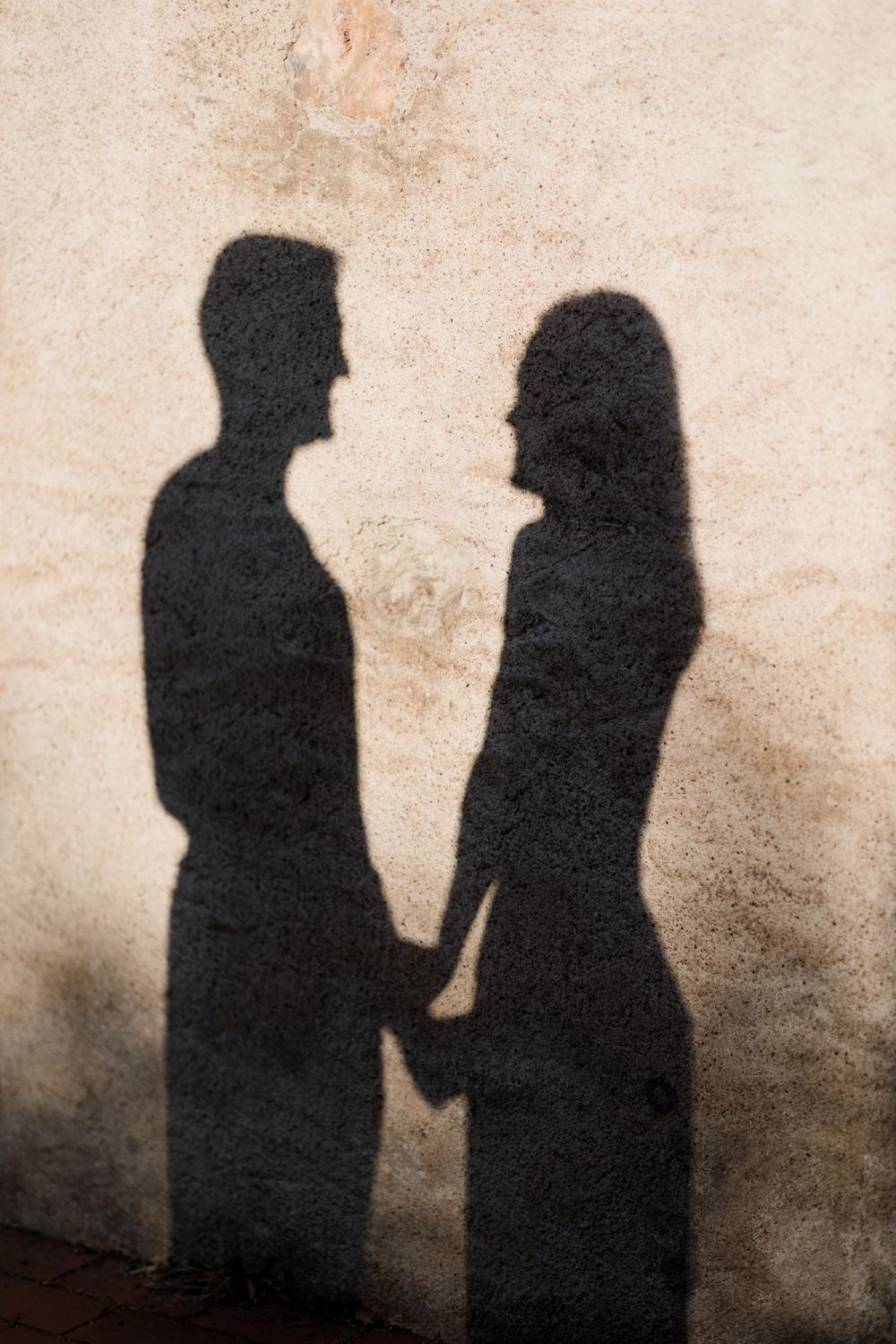 Silhouettes of a couple holding hands cast on a textured beige wall creating a romantic shadow effect. Seance couple Tours