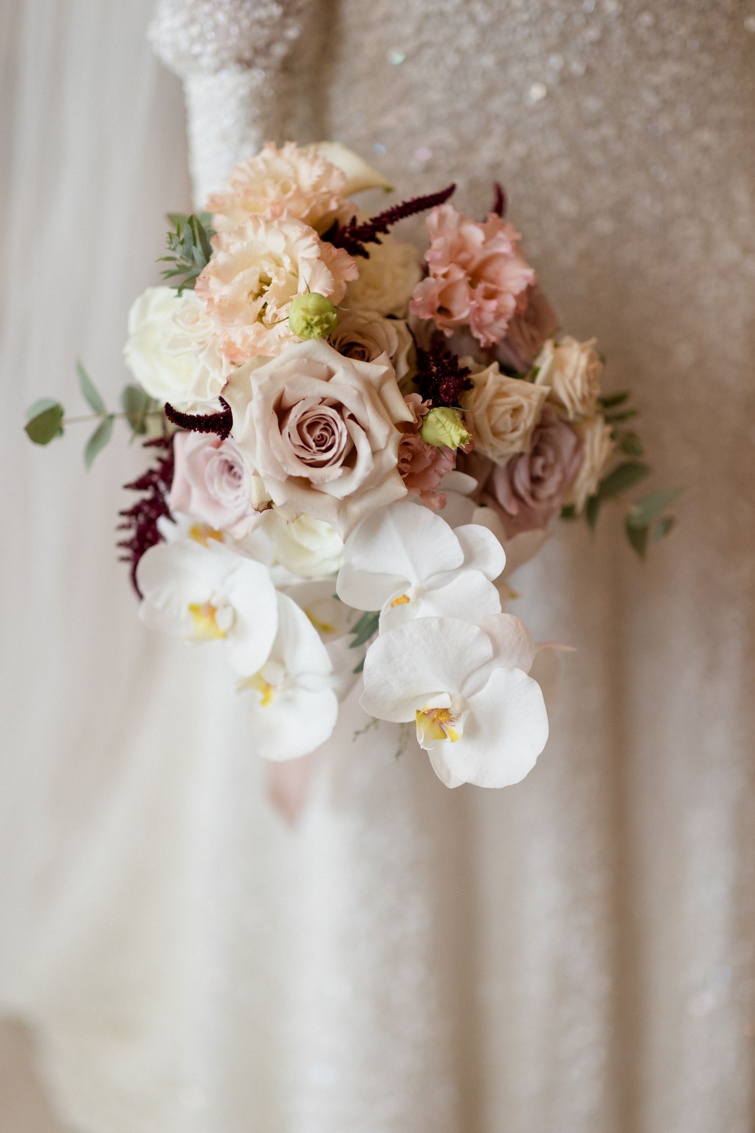 Elegant floral arrangement with soft pink roses, white orchids and delicate peach blooms against a light neutral background.
