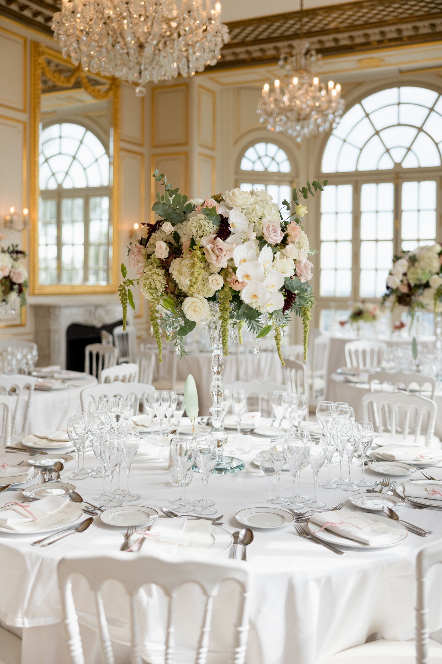 Elegant wedding reception tables with white linens, crystal chandeliers, and tall floral centerpieces in a grand ballroom. mariage grasse