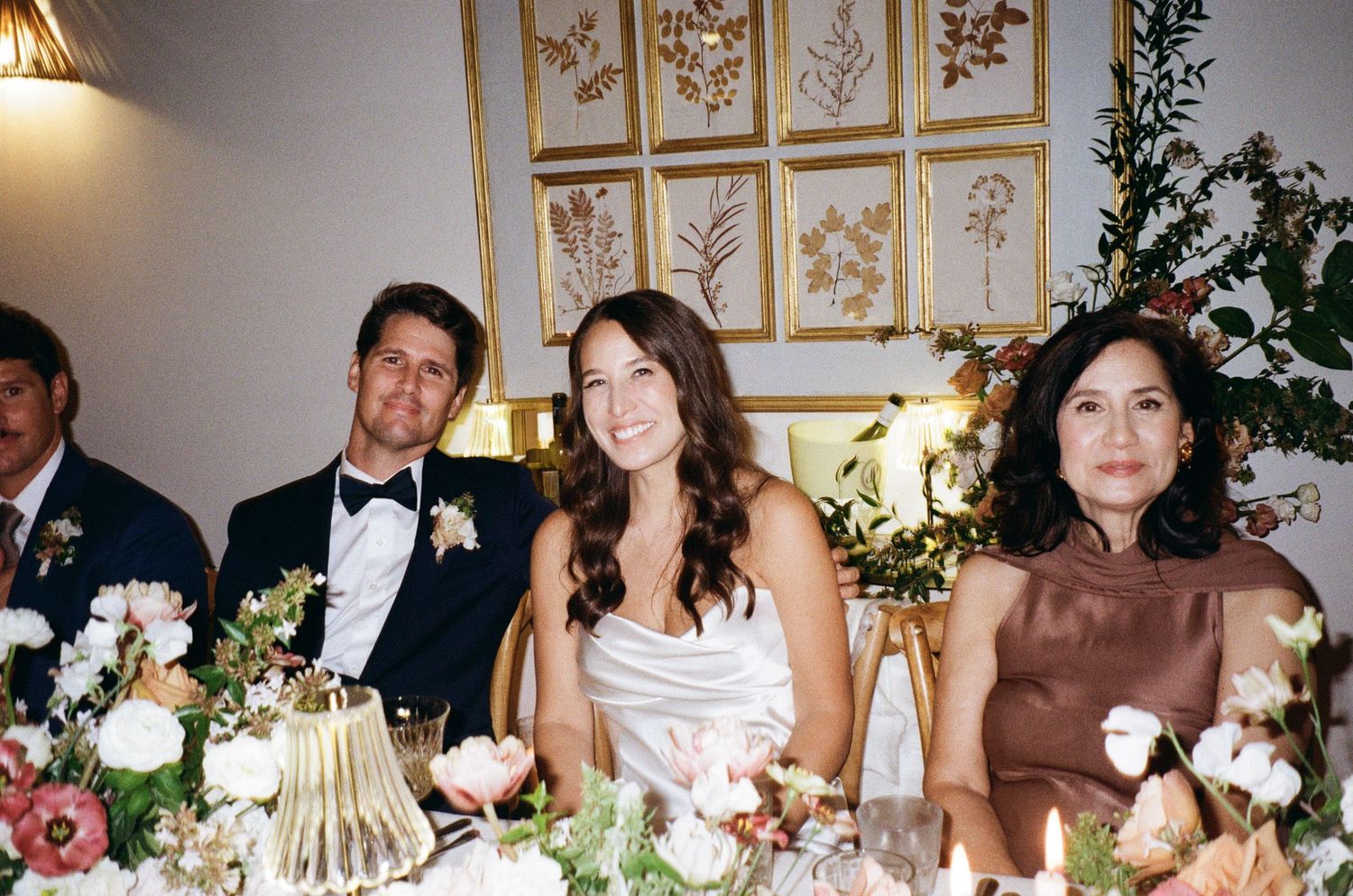 Wedding guests enjoying a reception dinner at elegantly decorated tables with floral centerpieces and golden decor.