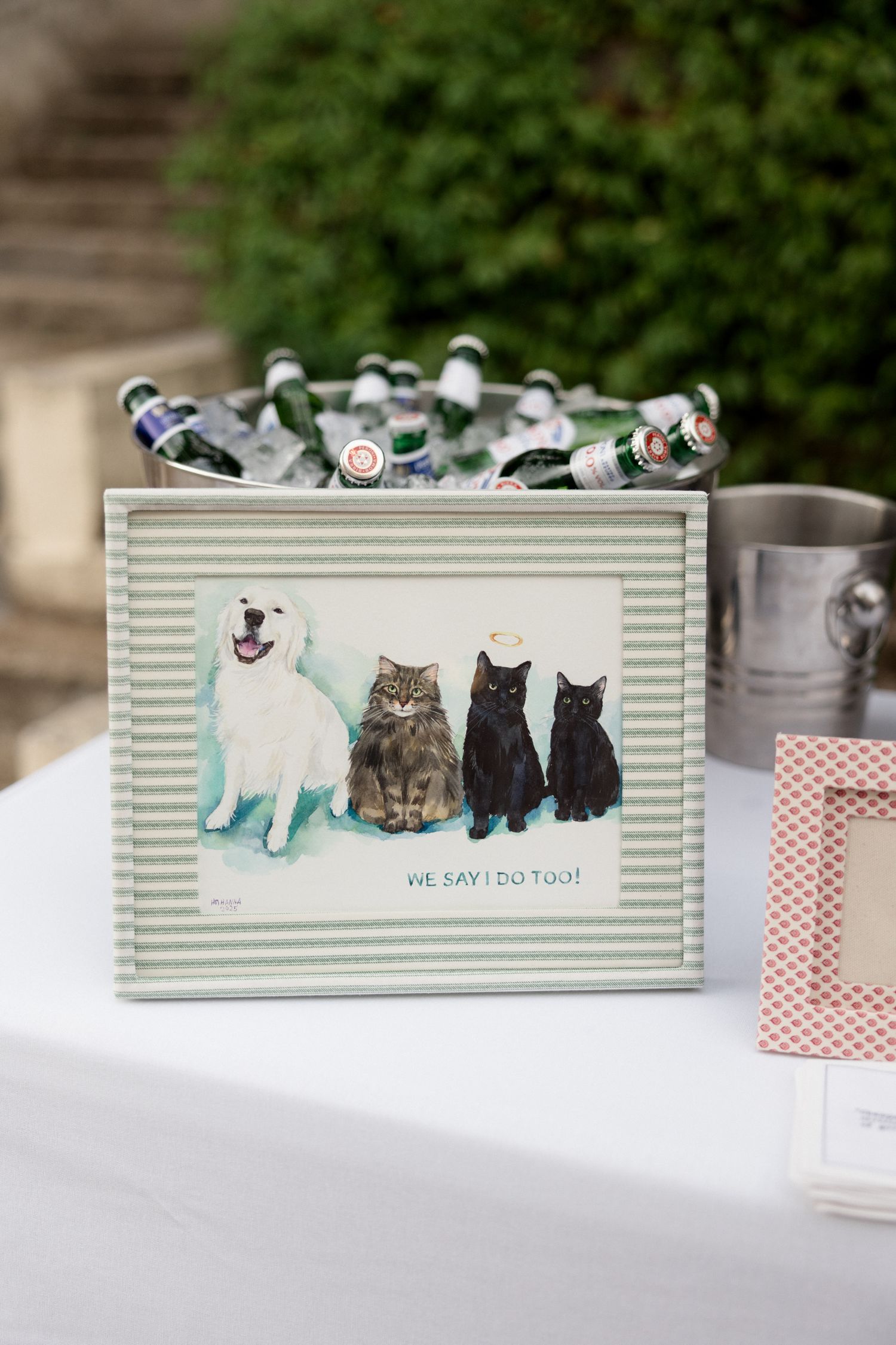 Decorative box with cats and dogs painted on the side sits on white table with party supplies and glass bottles.