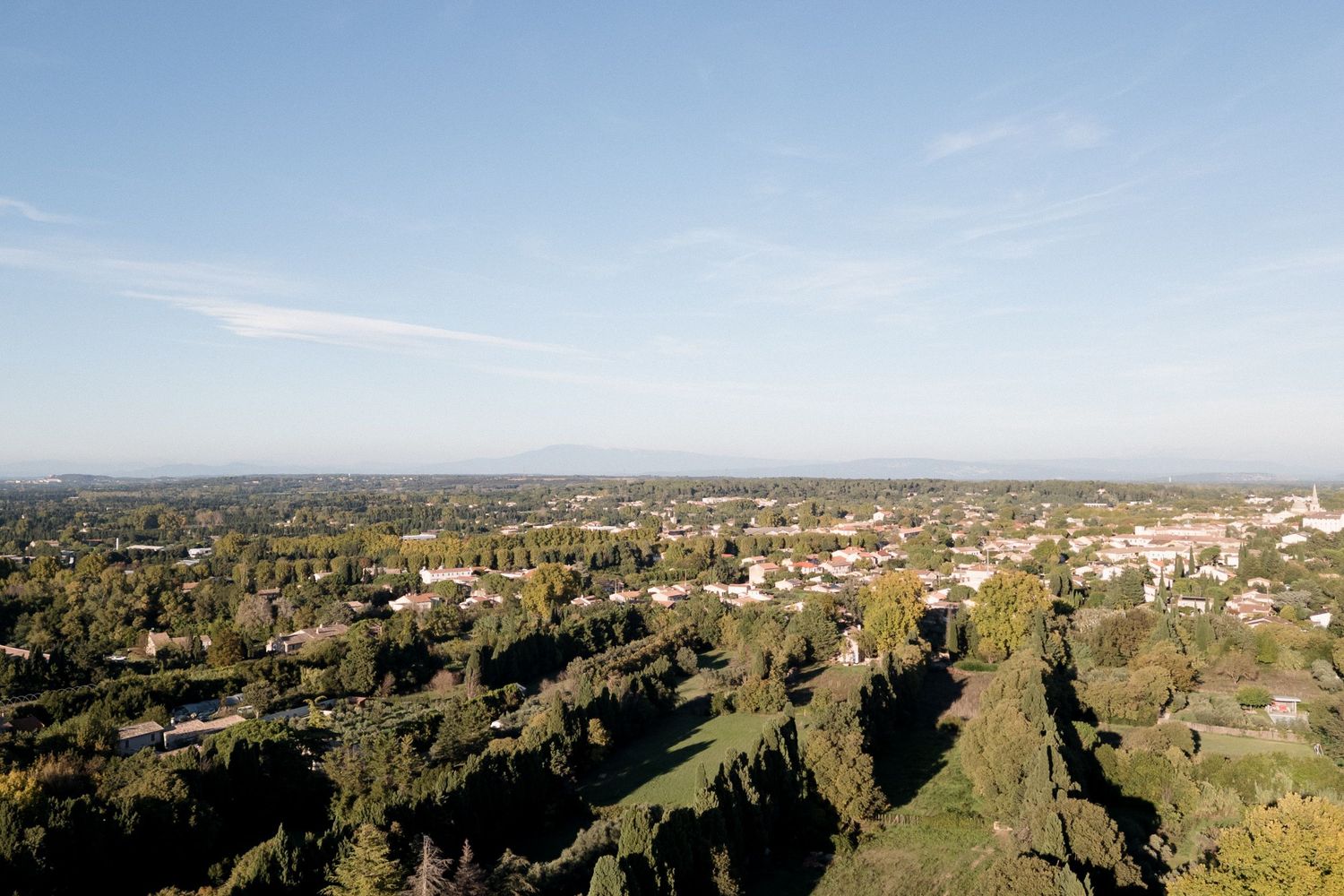 Panoramic aerial view of a suburban town nestled among green hills with mountains visible in the distance.