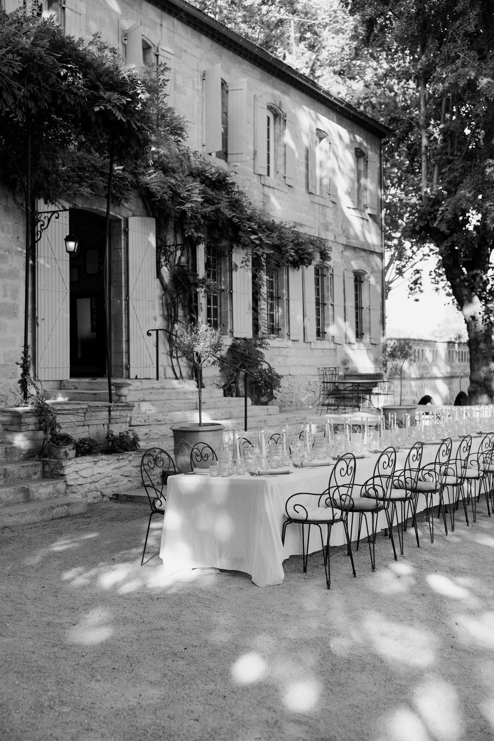 Black and white photo of an outdoor dining setup with iron chairs against a historic vine-covered building.