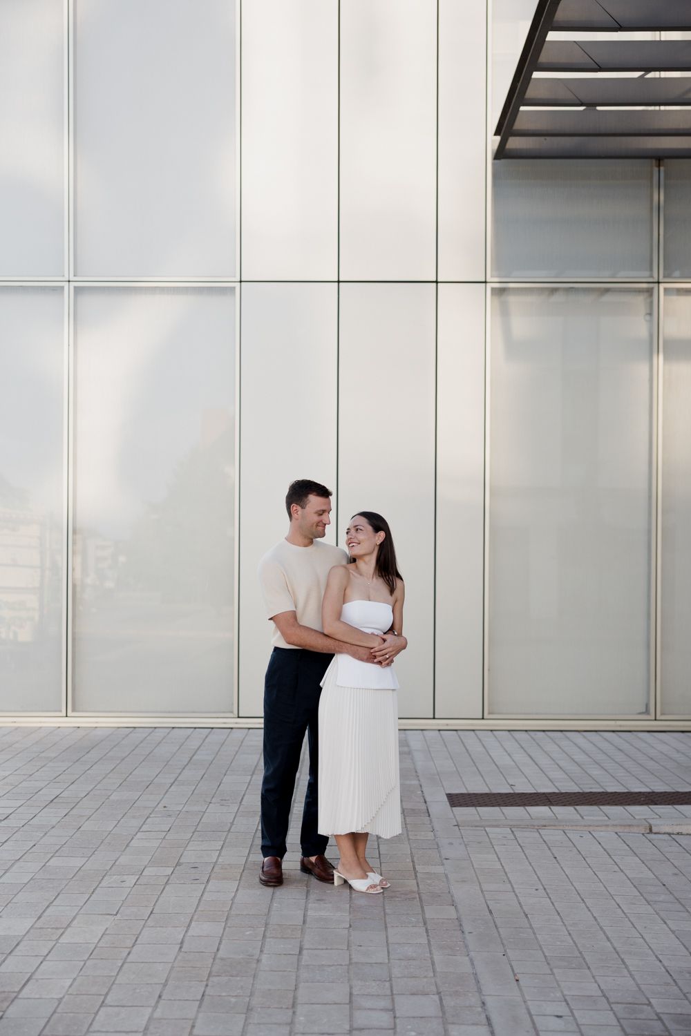 Couple in black and white attire sharing an intimate moment against a modern architectural backdrop.