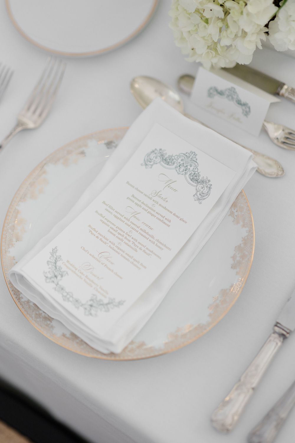 White and silver wedding invitations displayed on delicate blush-rimmed plates with ornate details. Château des 3 Fontaines wedding Provence
