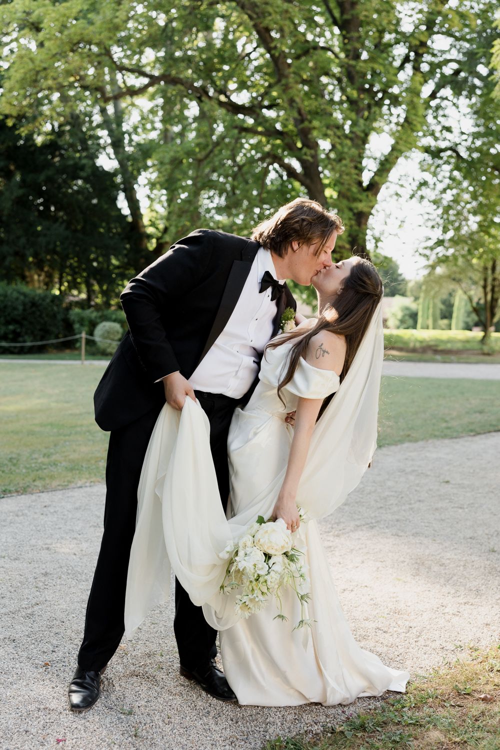 Romantic wedding scene captured in a series of dipping poses on a gravel path surrounded by greenery.