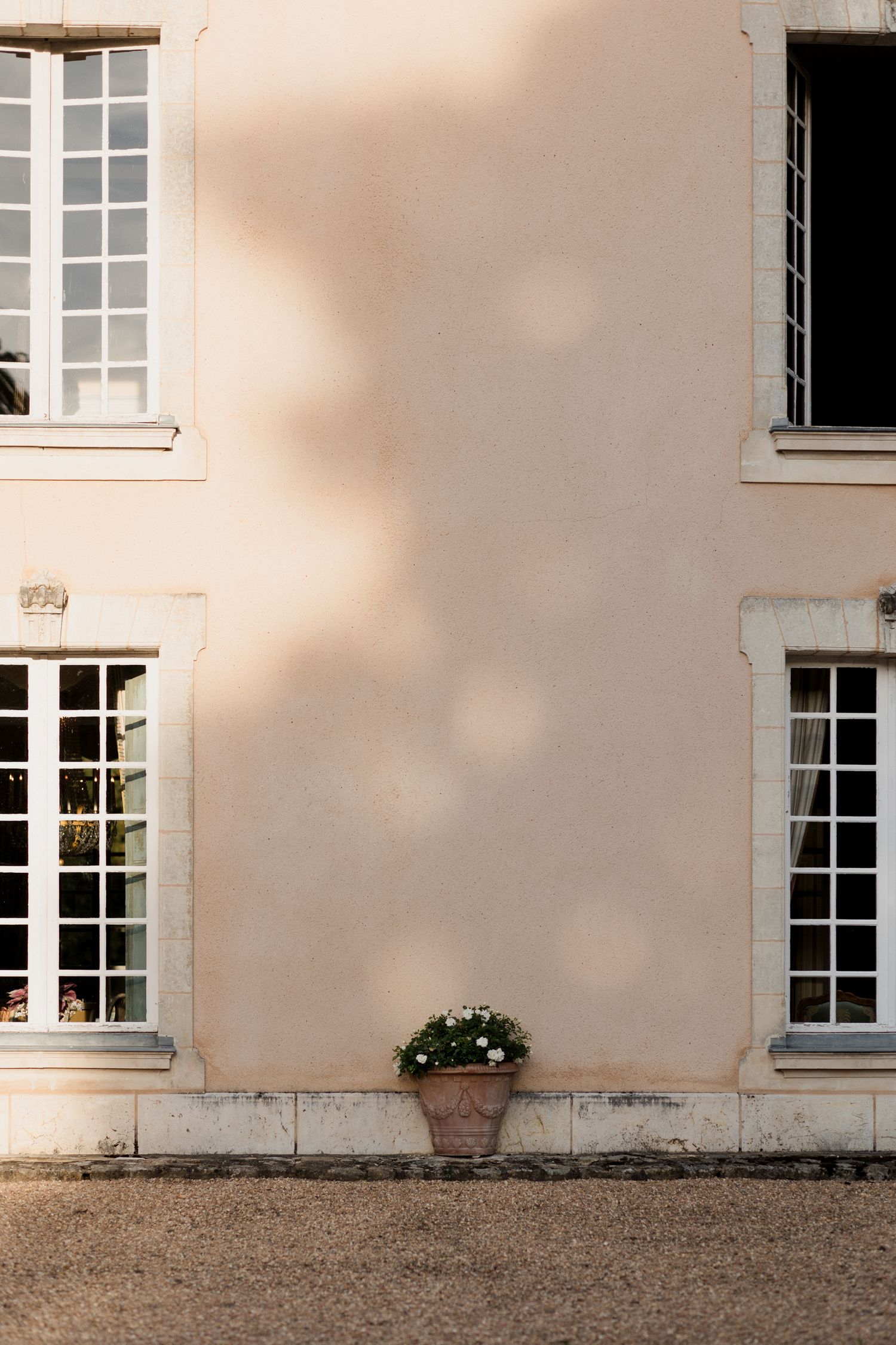 White windows with mullions line the exterior wall of a classic French country house with pale pink stucco finish.