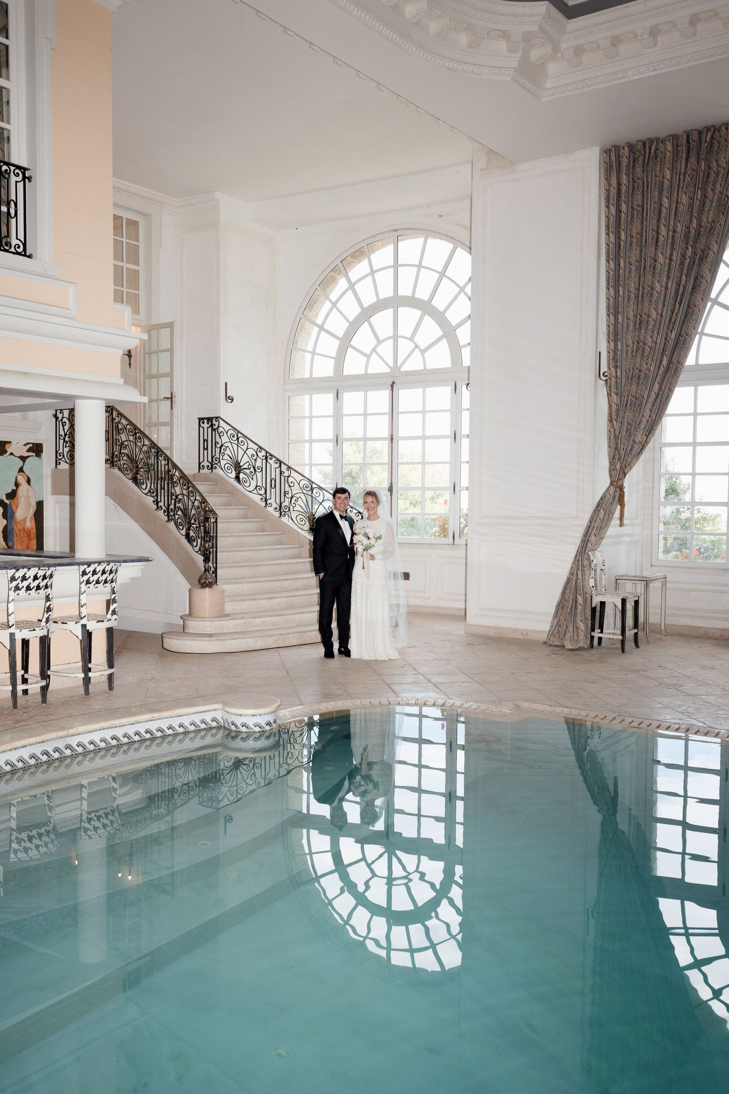 Elegant indoor swimming pool with arched windows and grand staircase in luxurious white interior setting. chateau saint goeorges