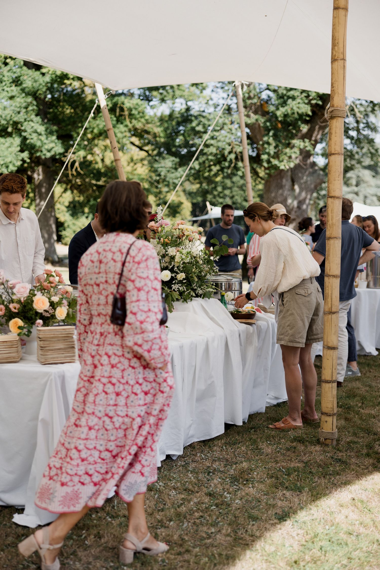 Guests mingling under a white tent at an outdoor garden party with white tablecloths.